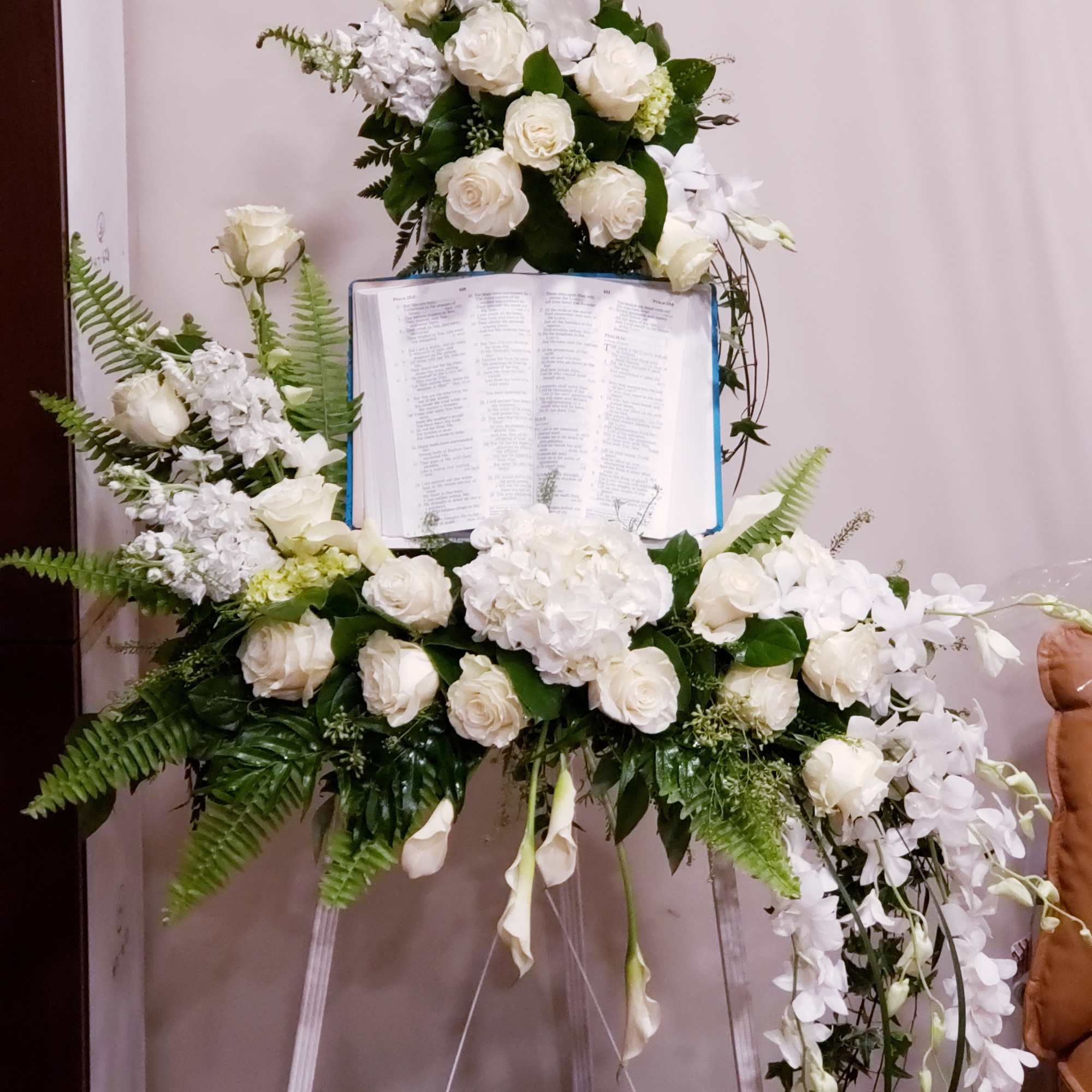 White floral funeral spray around an open book on an easel