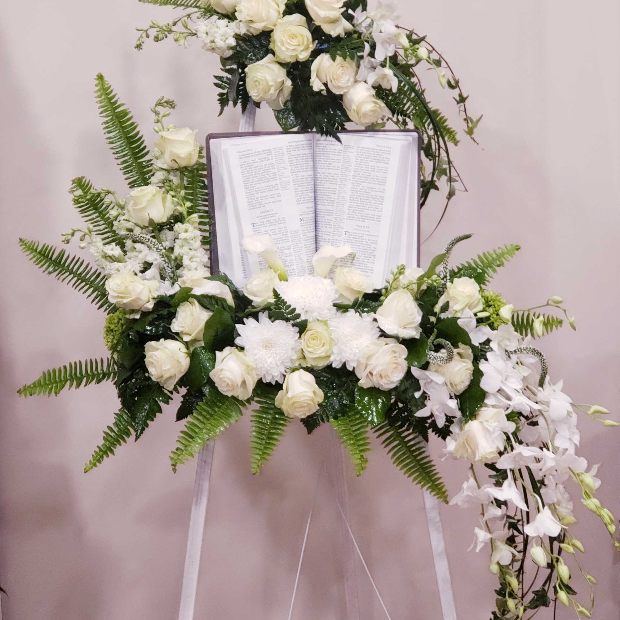 White floral funeral spray on an easel with an open book centerpiece