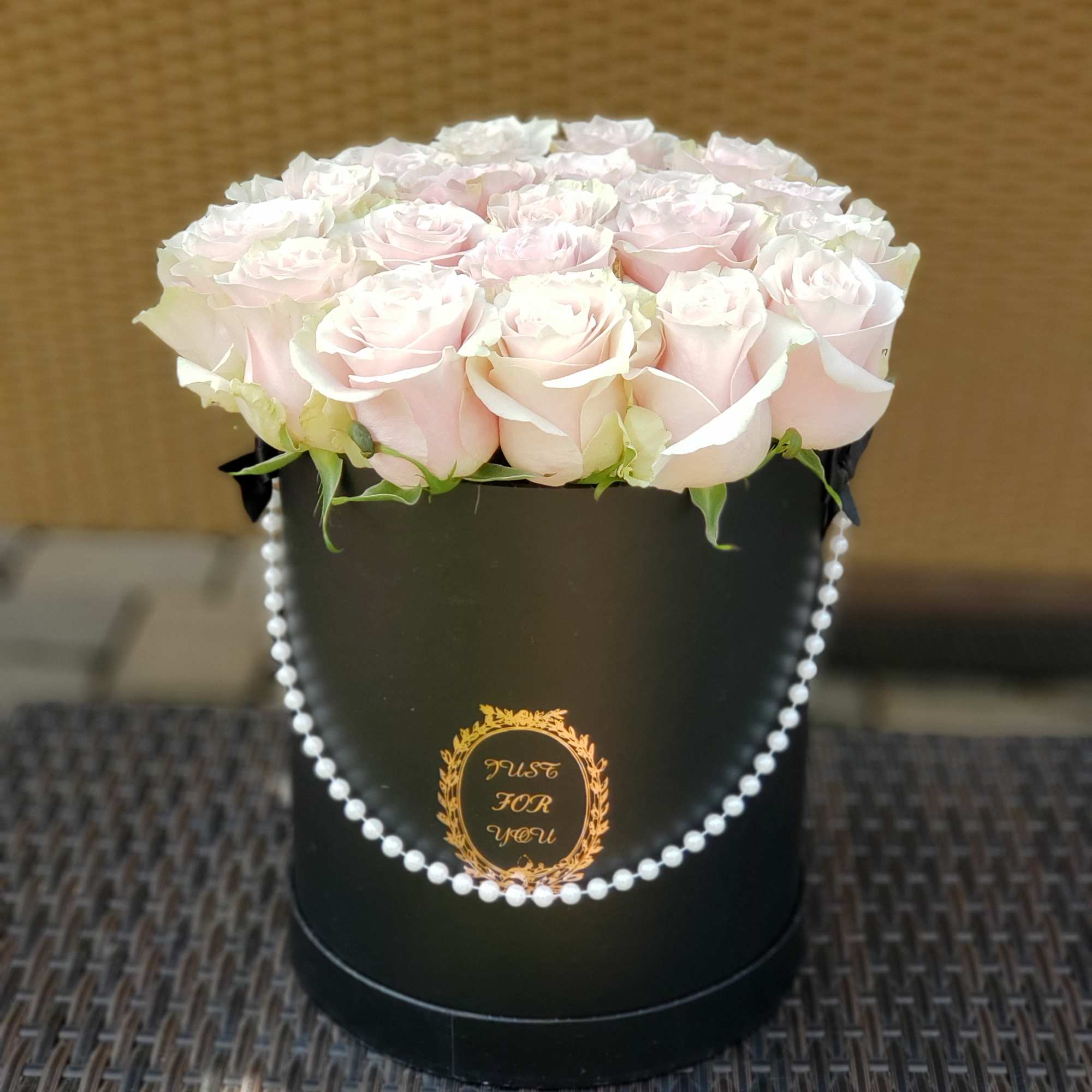 Pale pink roses arranged in a black round box with pearl trim
