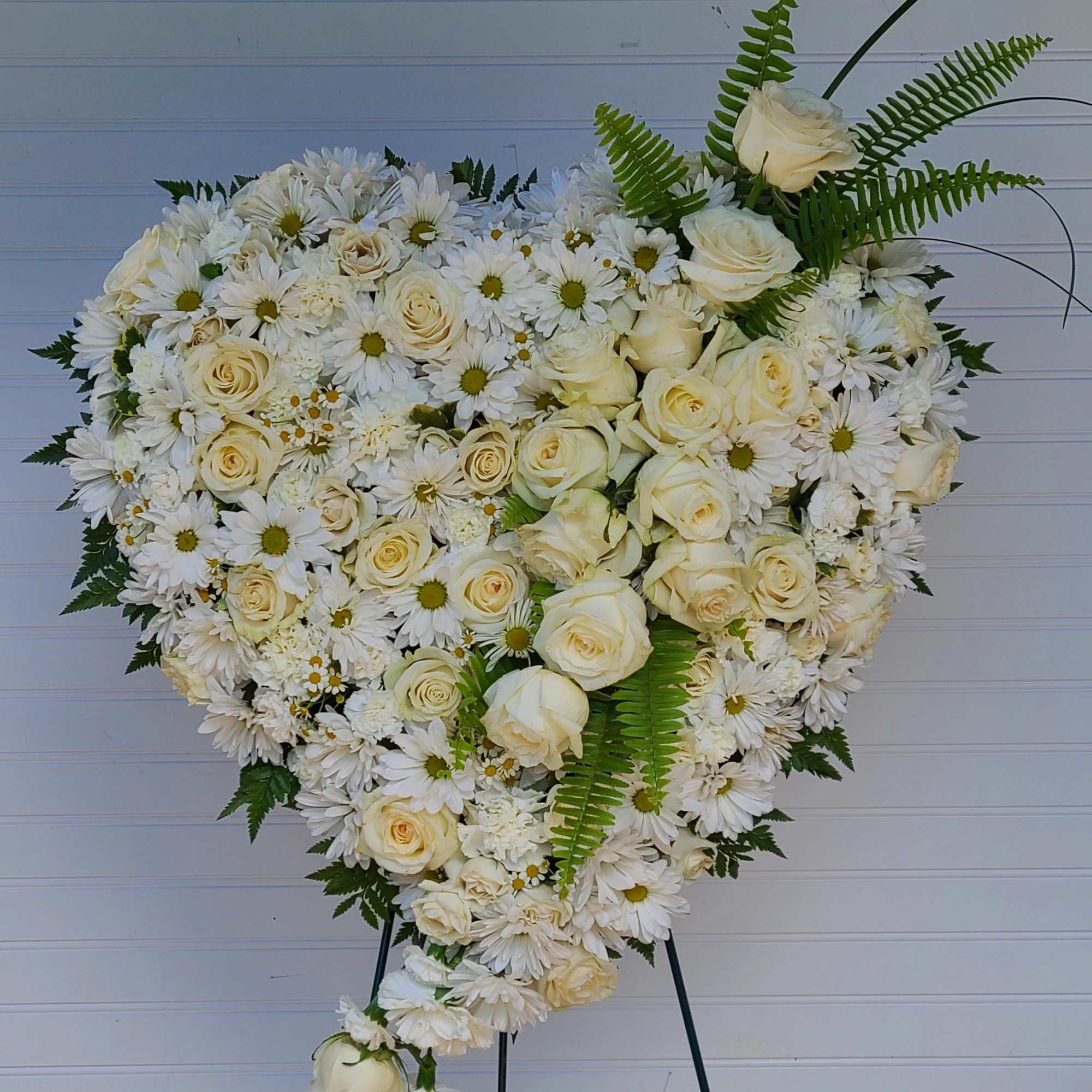 Heart-shaped white floral spray with roses and daisies on an easel