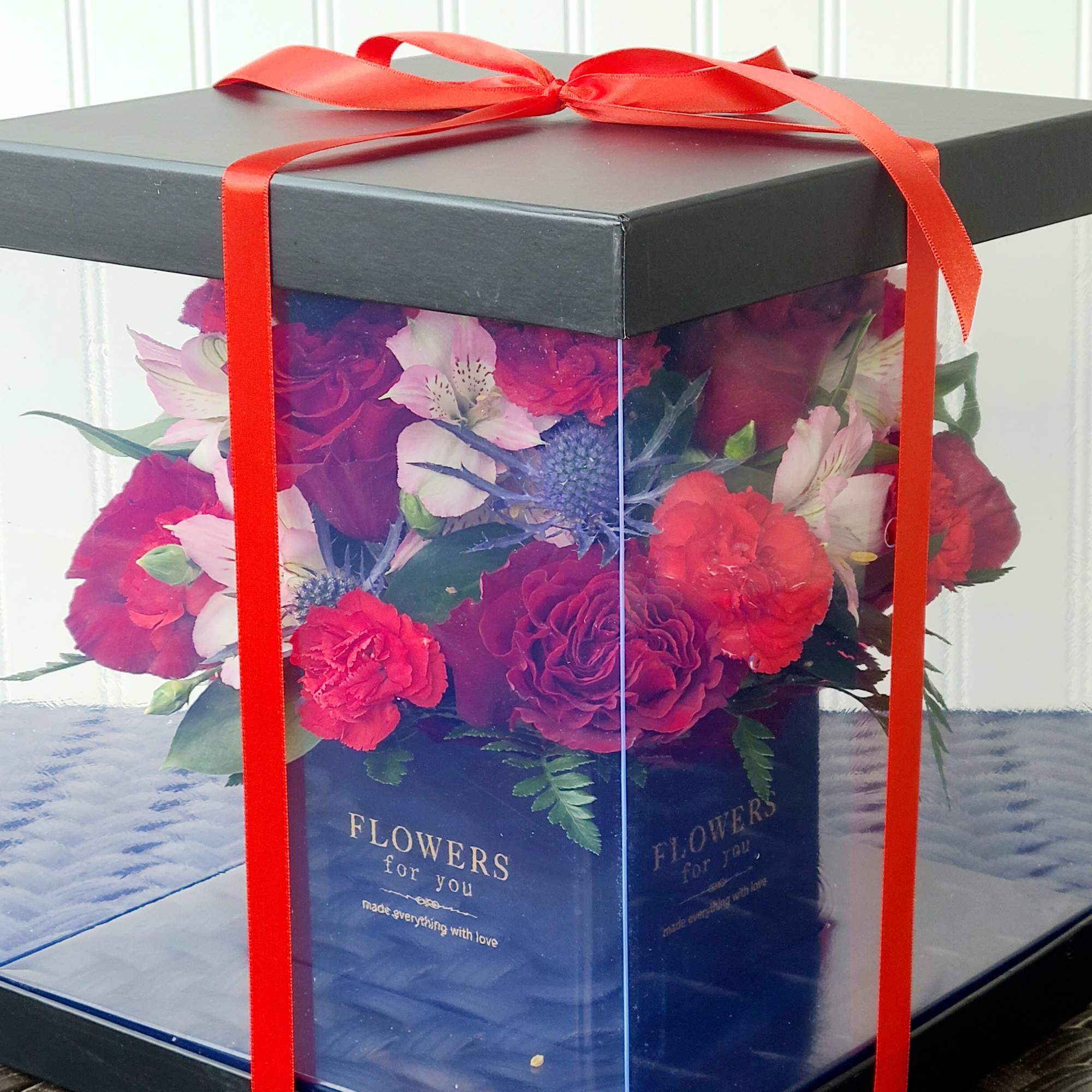 Boxed bouquet of red and pink flowers tied with a red ribbon