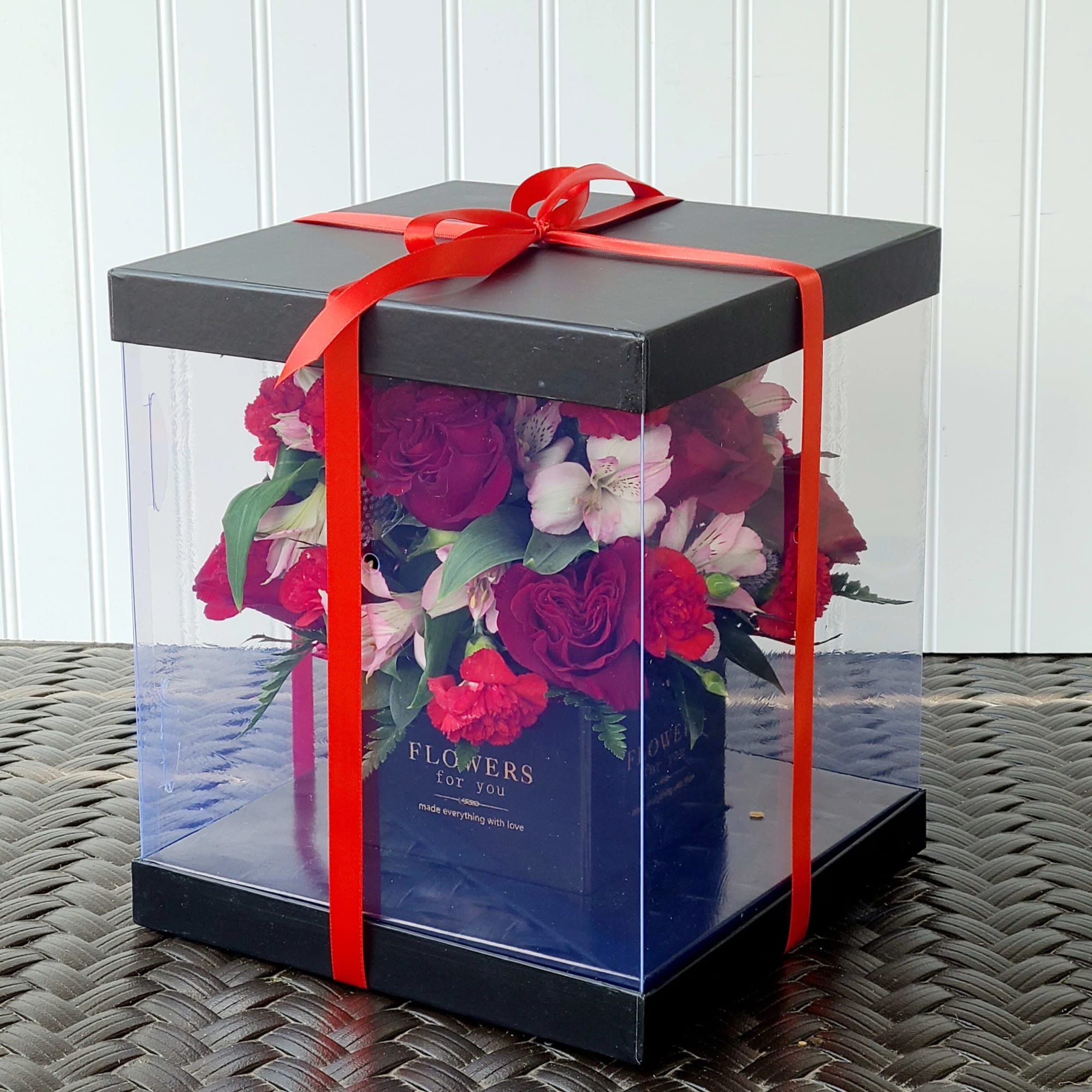 Boxed bouquet of red and pink flowers tied with a red ribbon