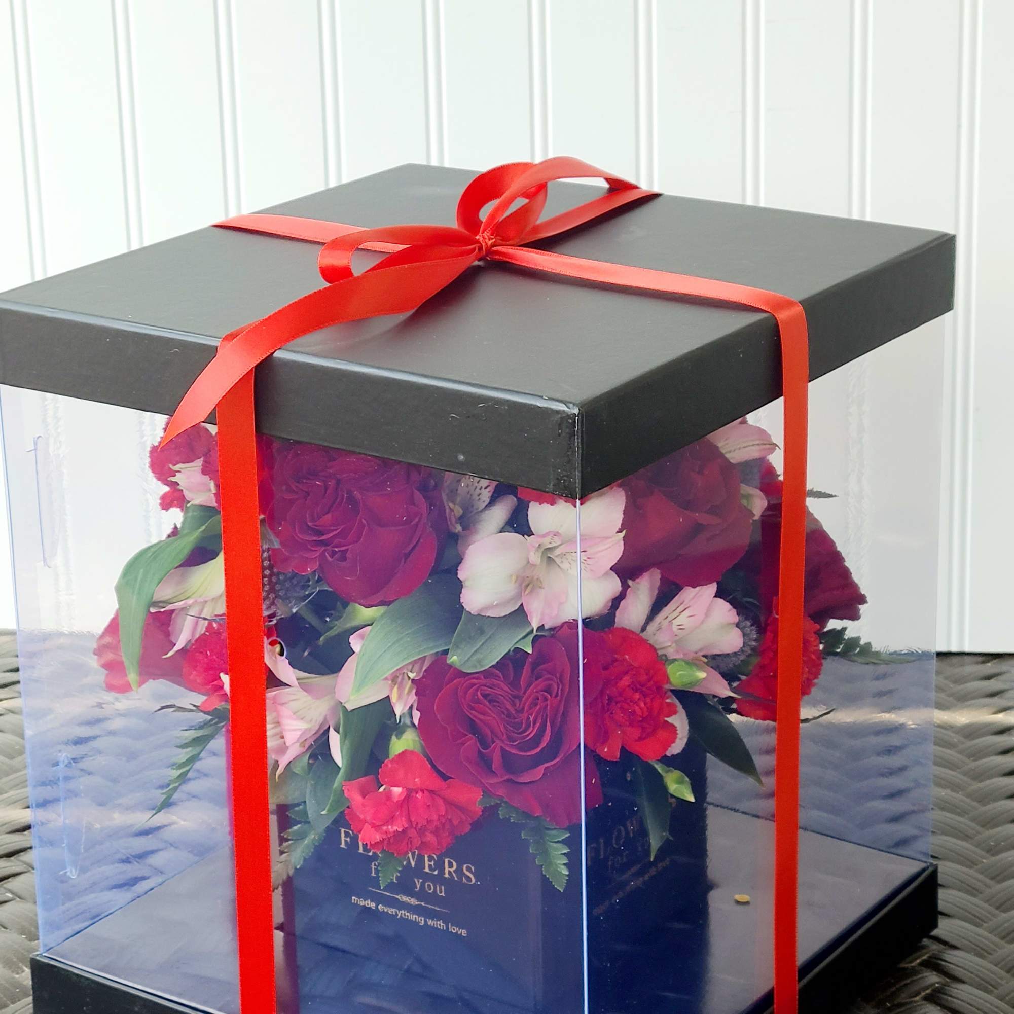 Red and pink flower arrangement in a clear gift box with a red ribbon