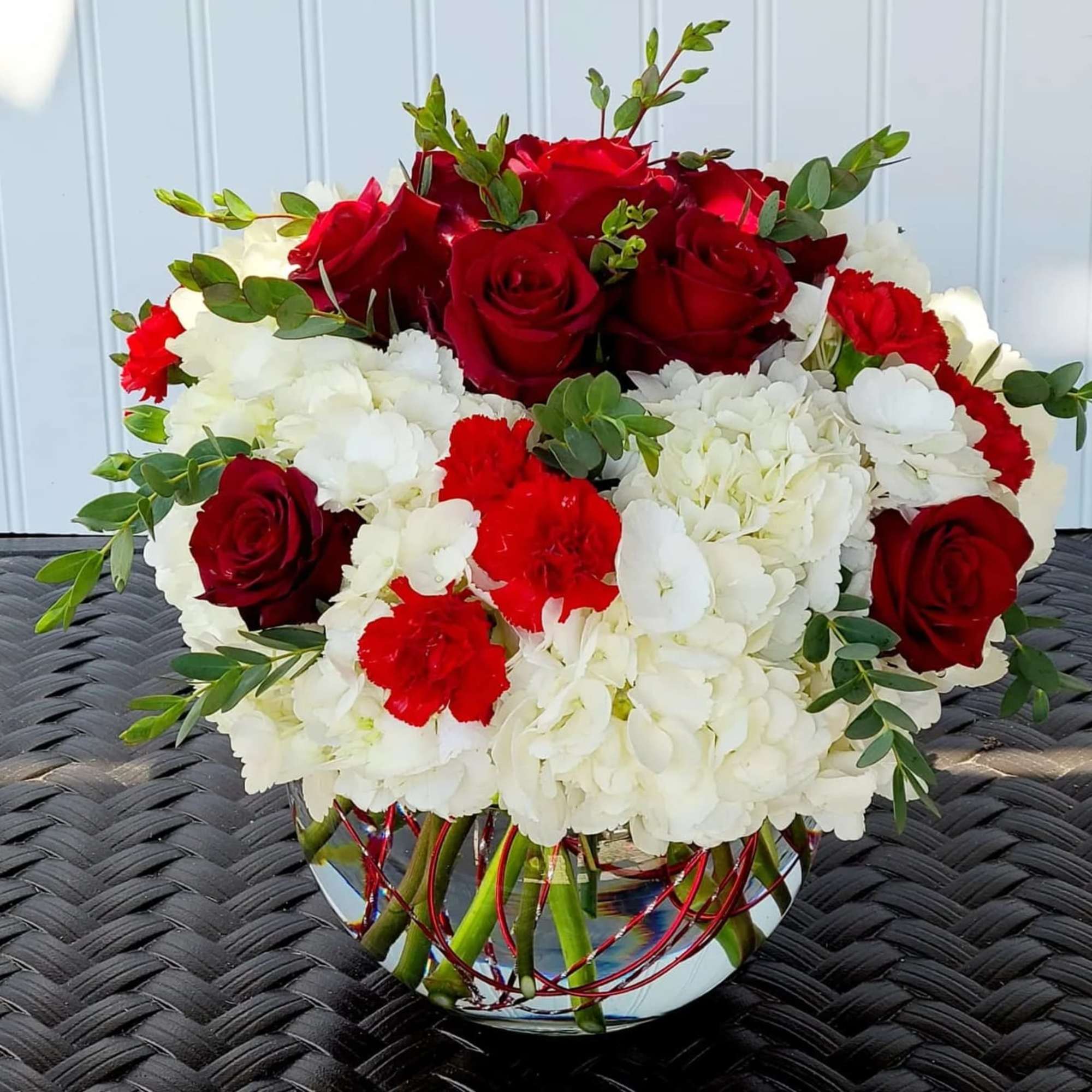 Red roses and white hydrangeas in a glass vase with greenery