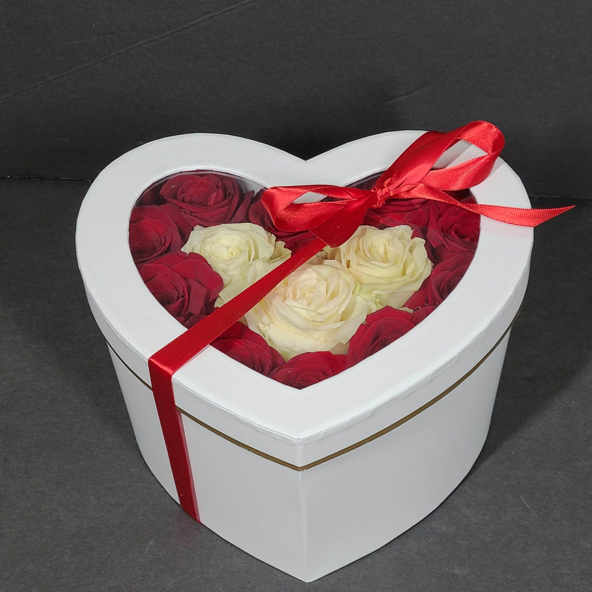 Heart-shaped white box filled with red and cream roses, tied with a red ribbon