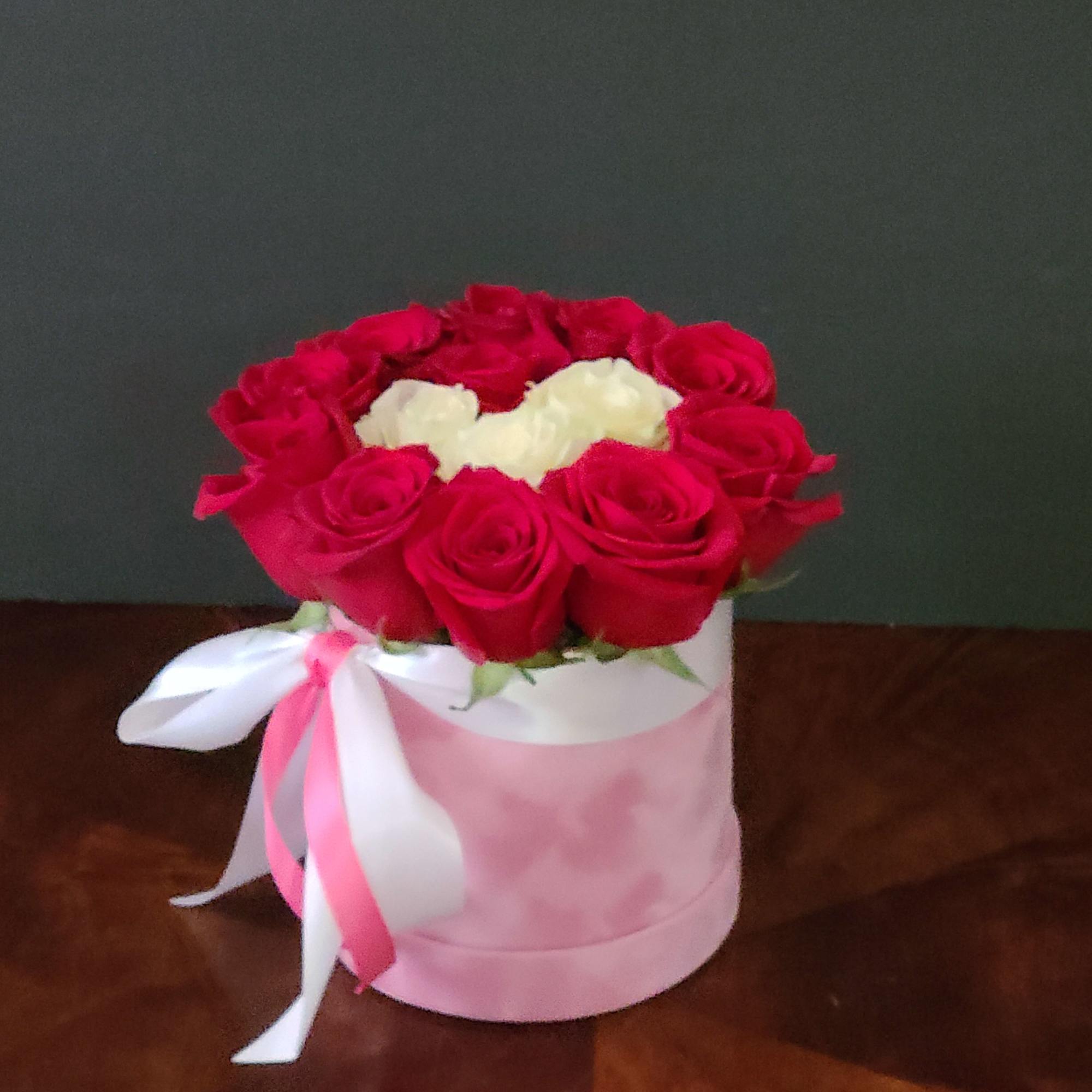 Red and white roses arranged in a pink hat box with ribbon