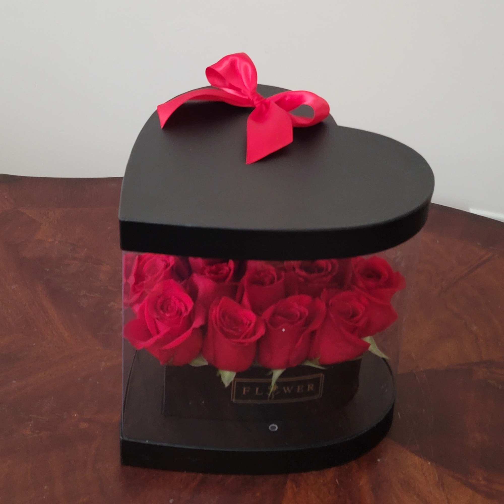 Red roses in a heart-shaped black box with a pink ribbon