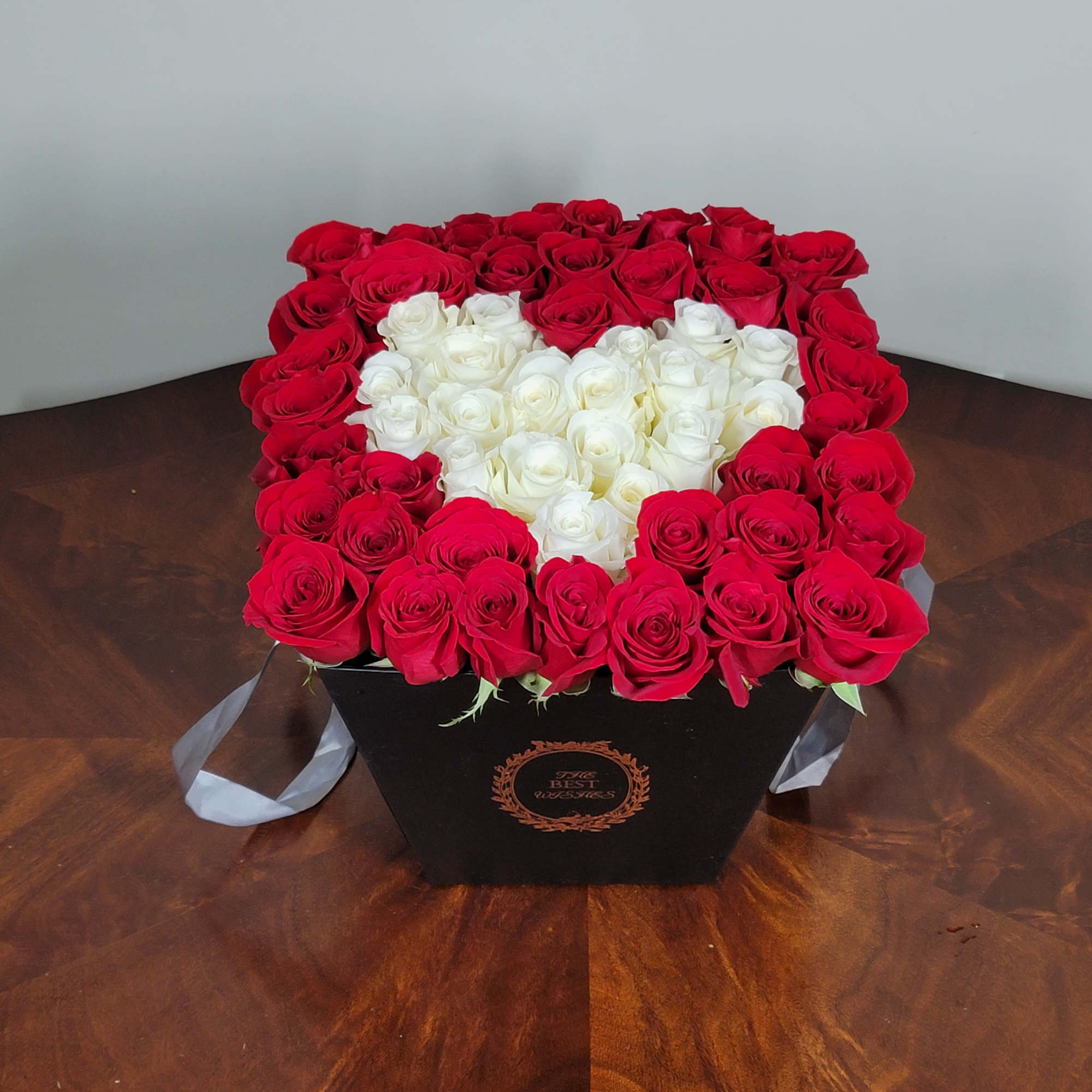 Heart-shaped box of red and white roses on a wooden table