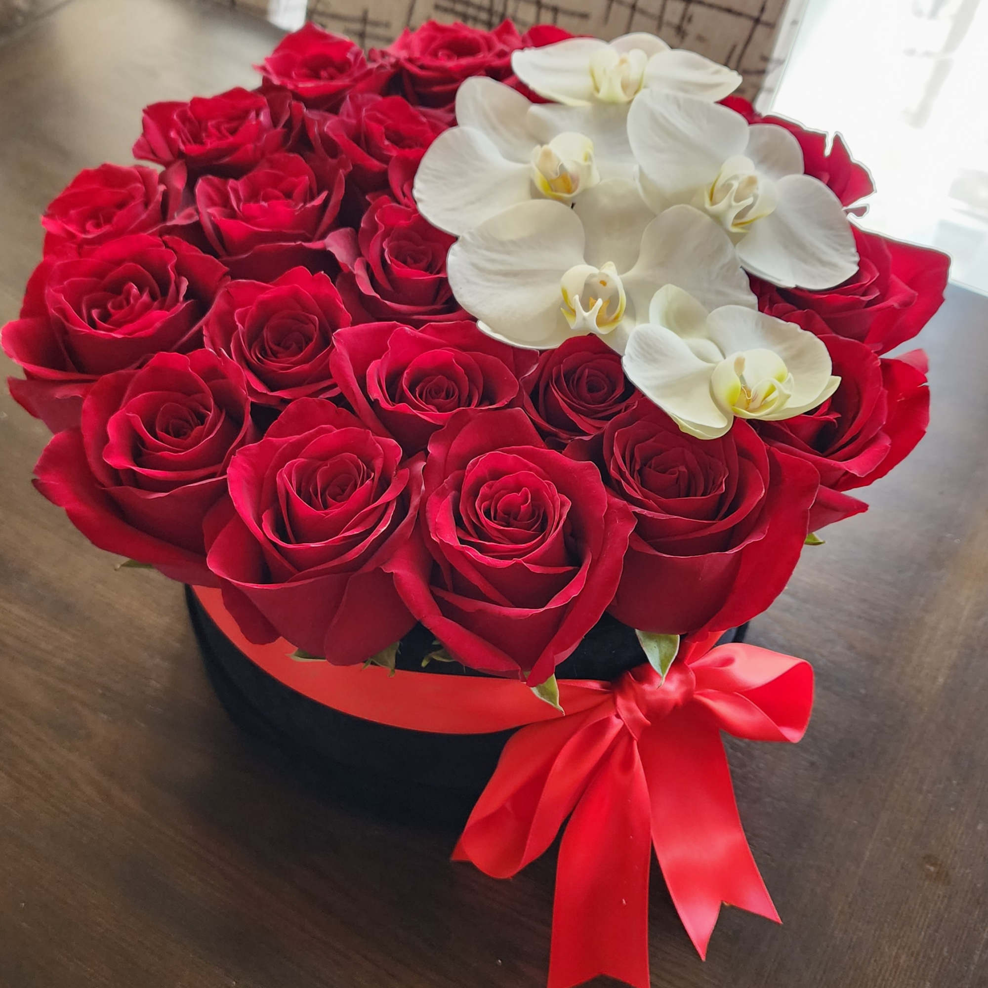 Red roses and white orchids arranged in a round black box with a red ribbon