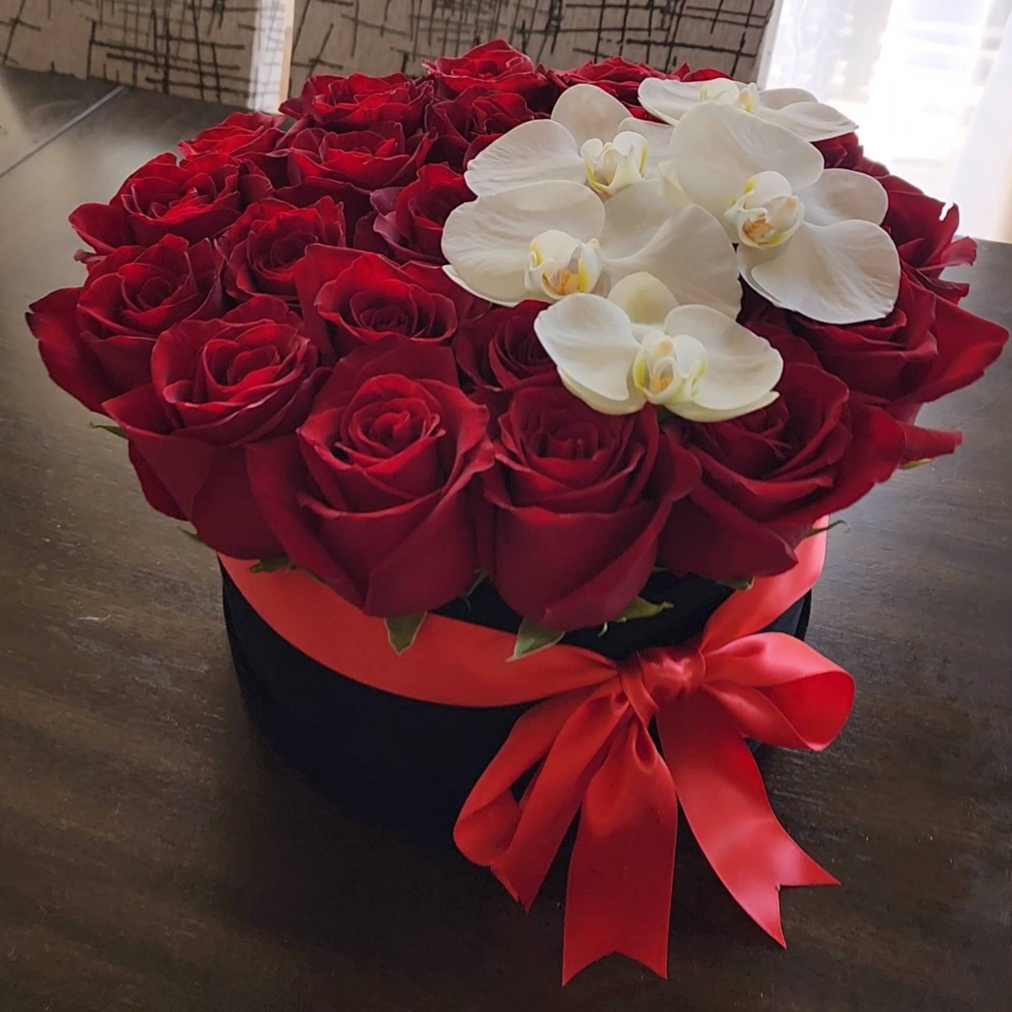 Red roses arranged in a black hat box with white orchids and a red ribbon