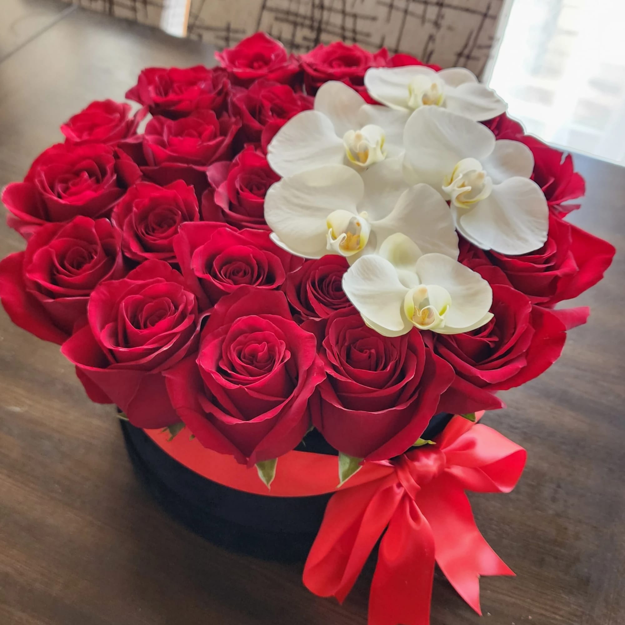 Red roses with white orchids in a round black box tied with a red ribbon