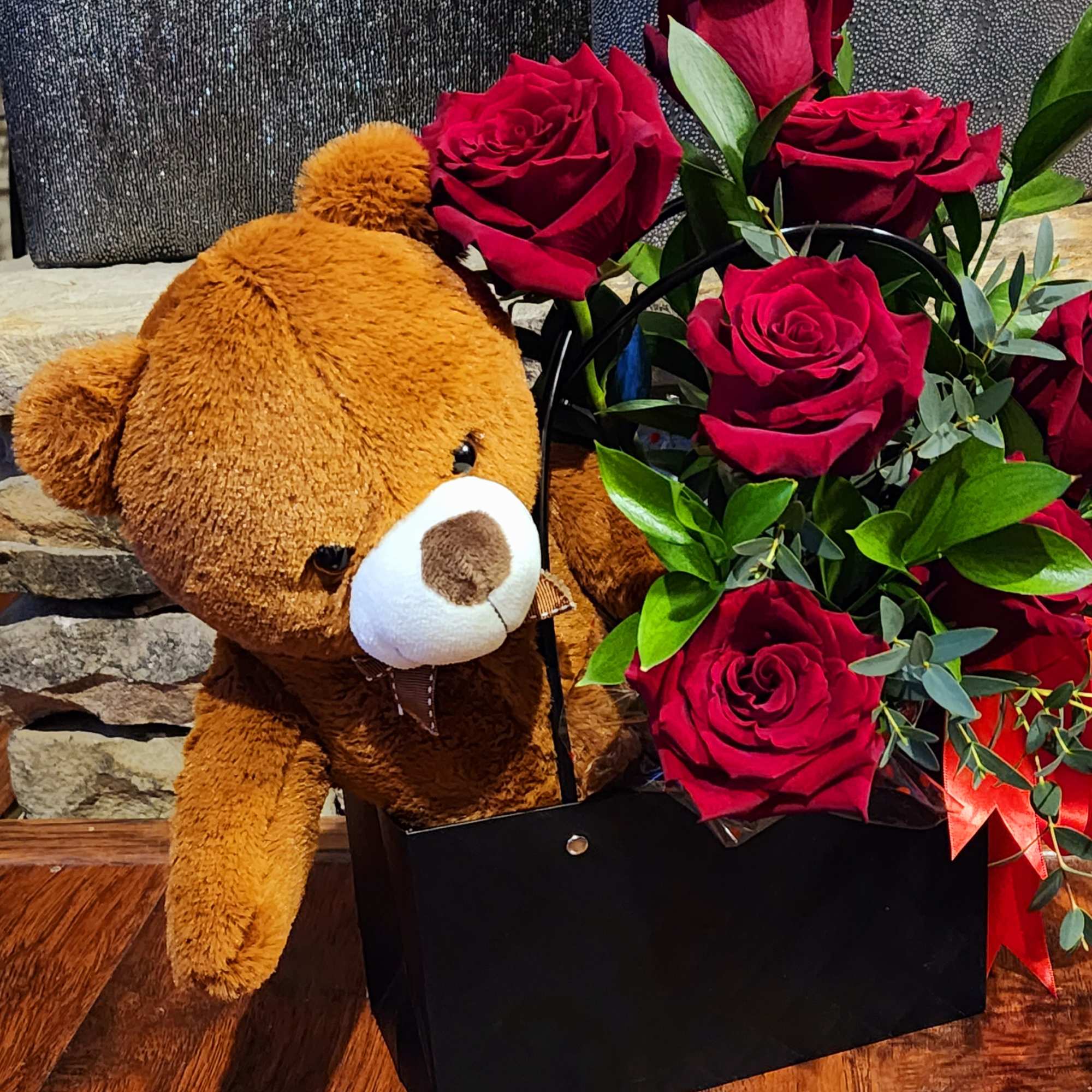 Teddy bear beside a black box of red roses