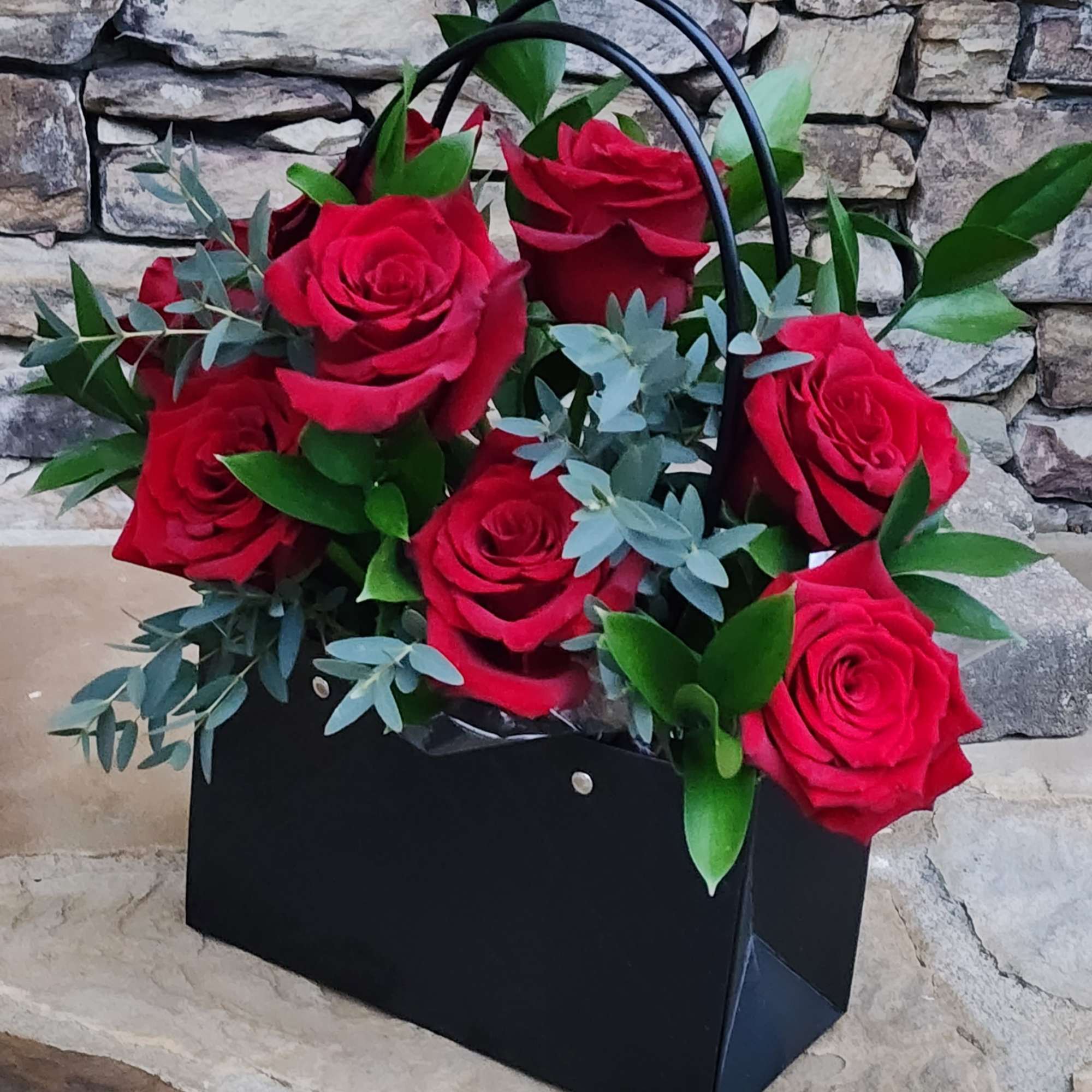 Black gift bag filled with red roses and greenery