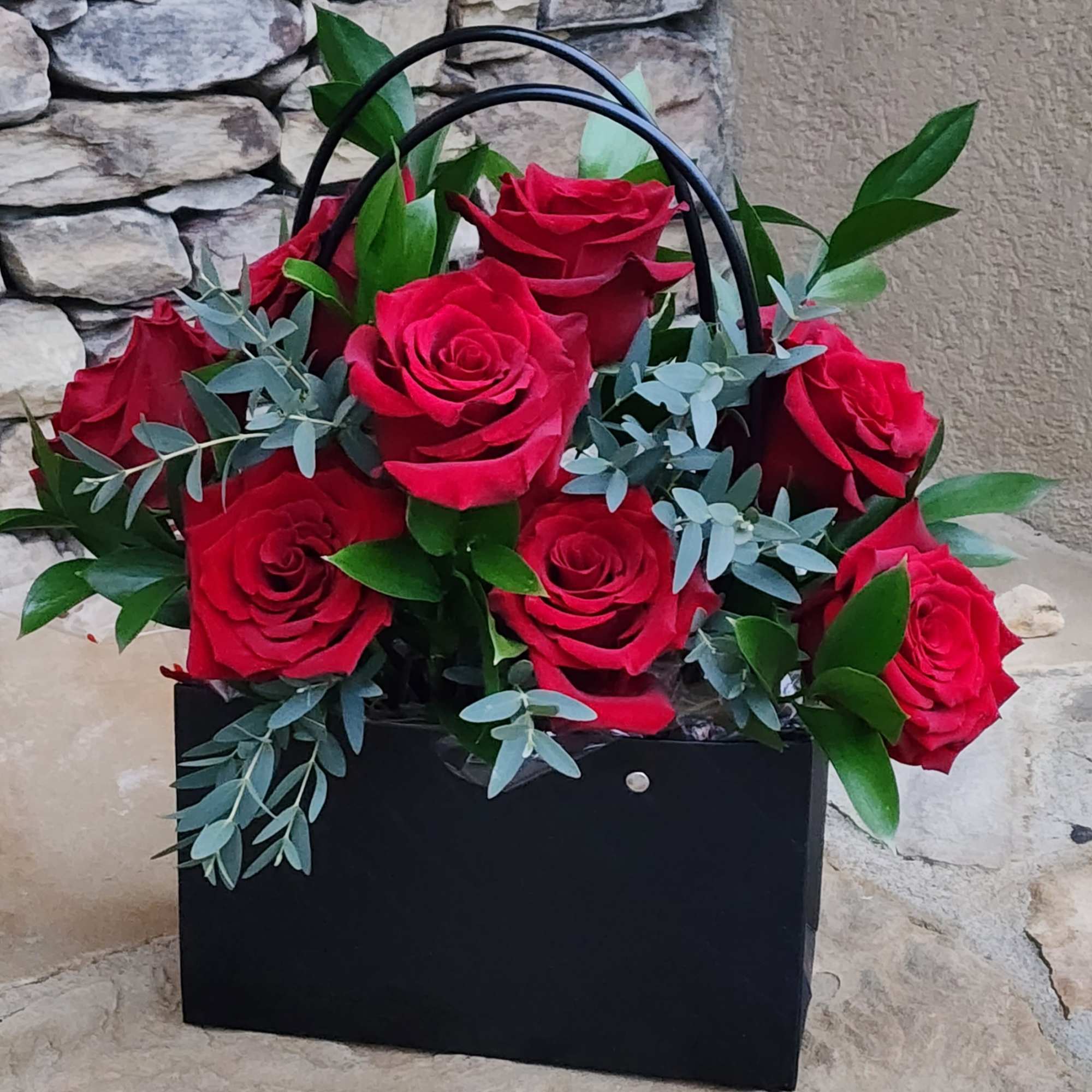 Black gift bag with red roses and blue-green foliage
