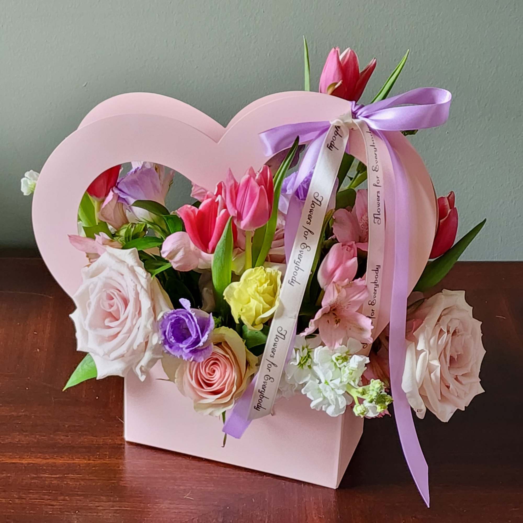 Pink heart-shaped box with mixed flowers and a lavender ribbon