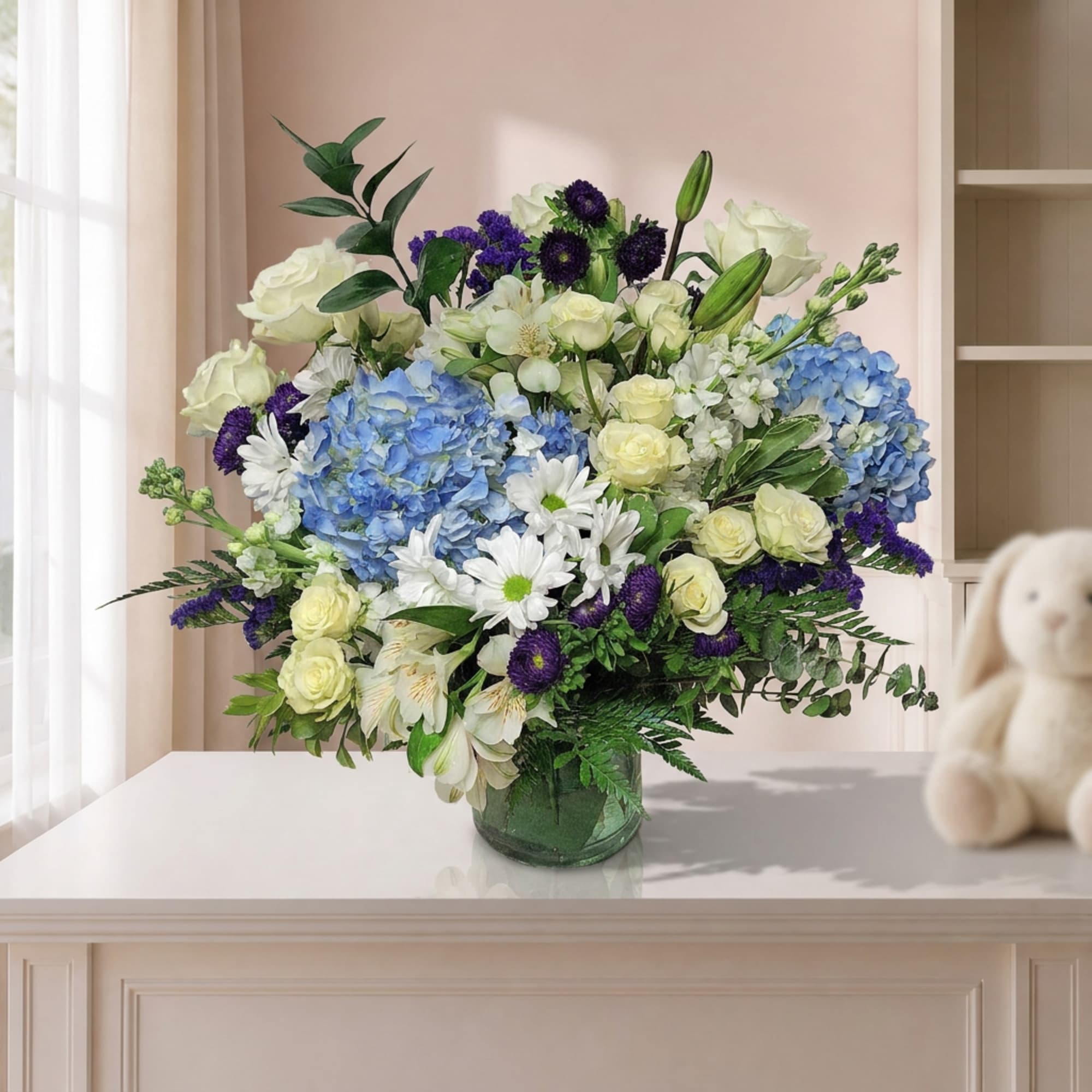 Bouquet of blue hydrangeas, white roses, and purple flowers in a glass vase