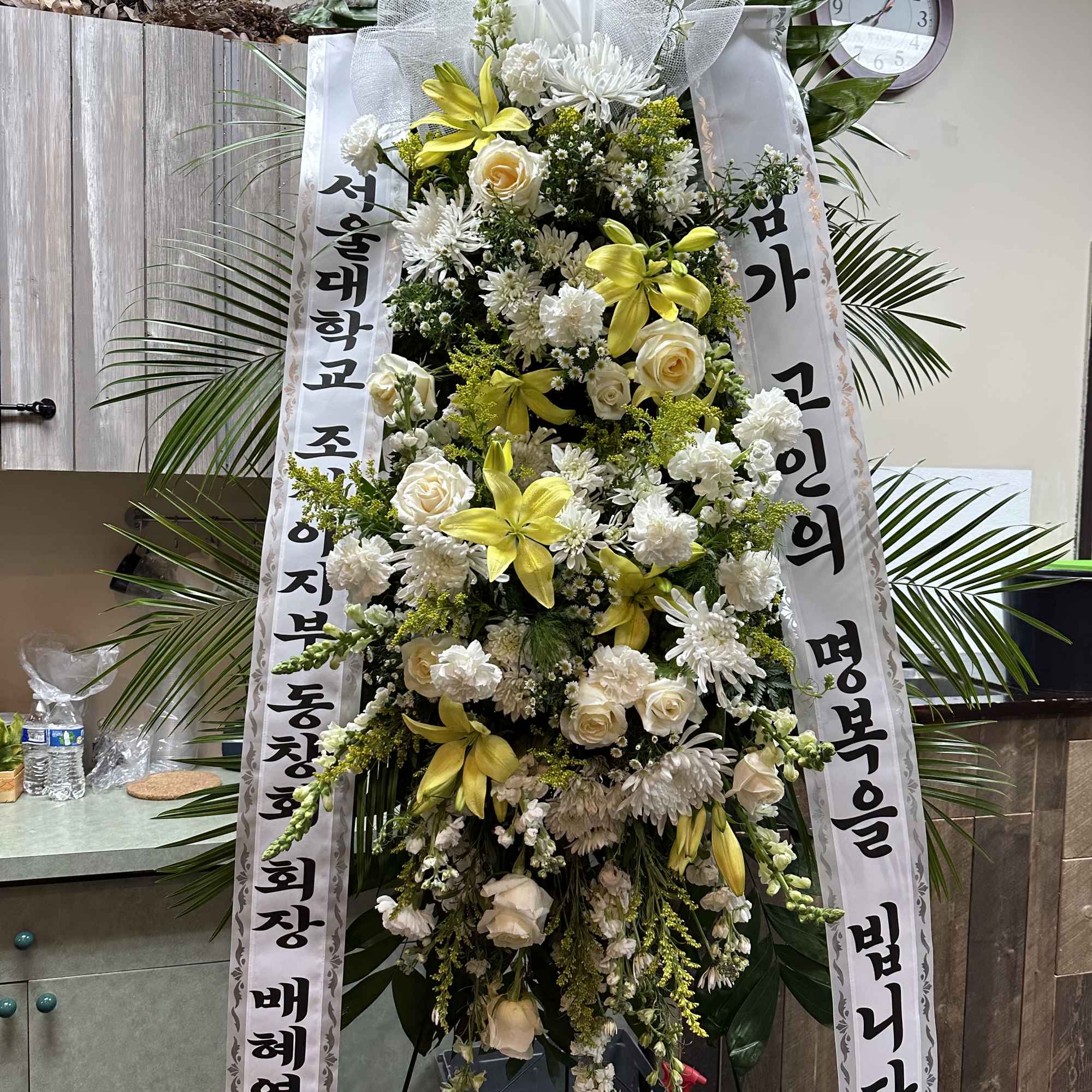 Tall standing floral spray with white and yellow flowers and ribbon banners