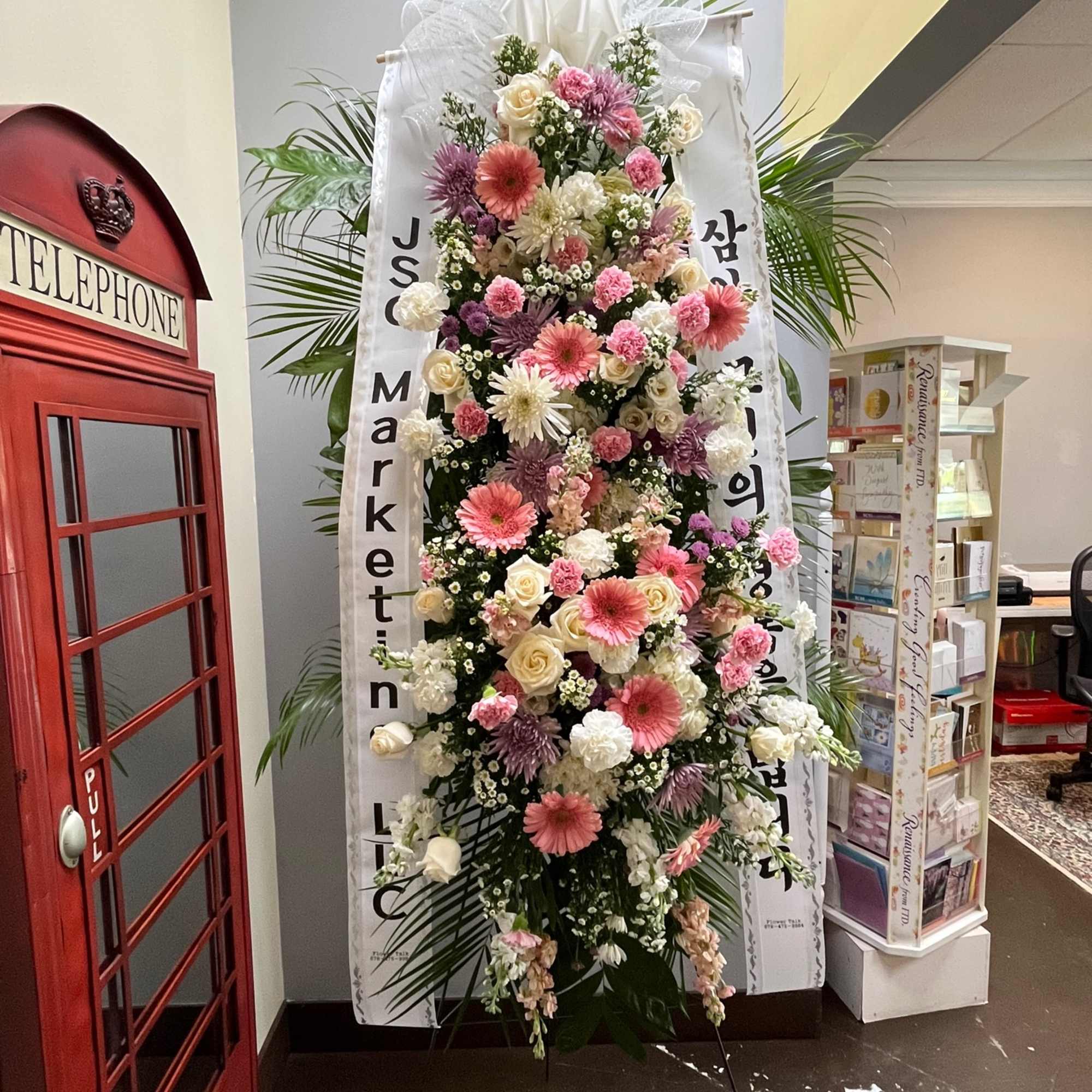Tall standing floral spray with pink, white, and lavender blooms on a white ribboned easel