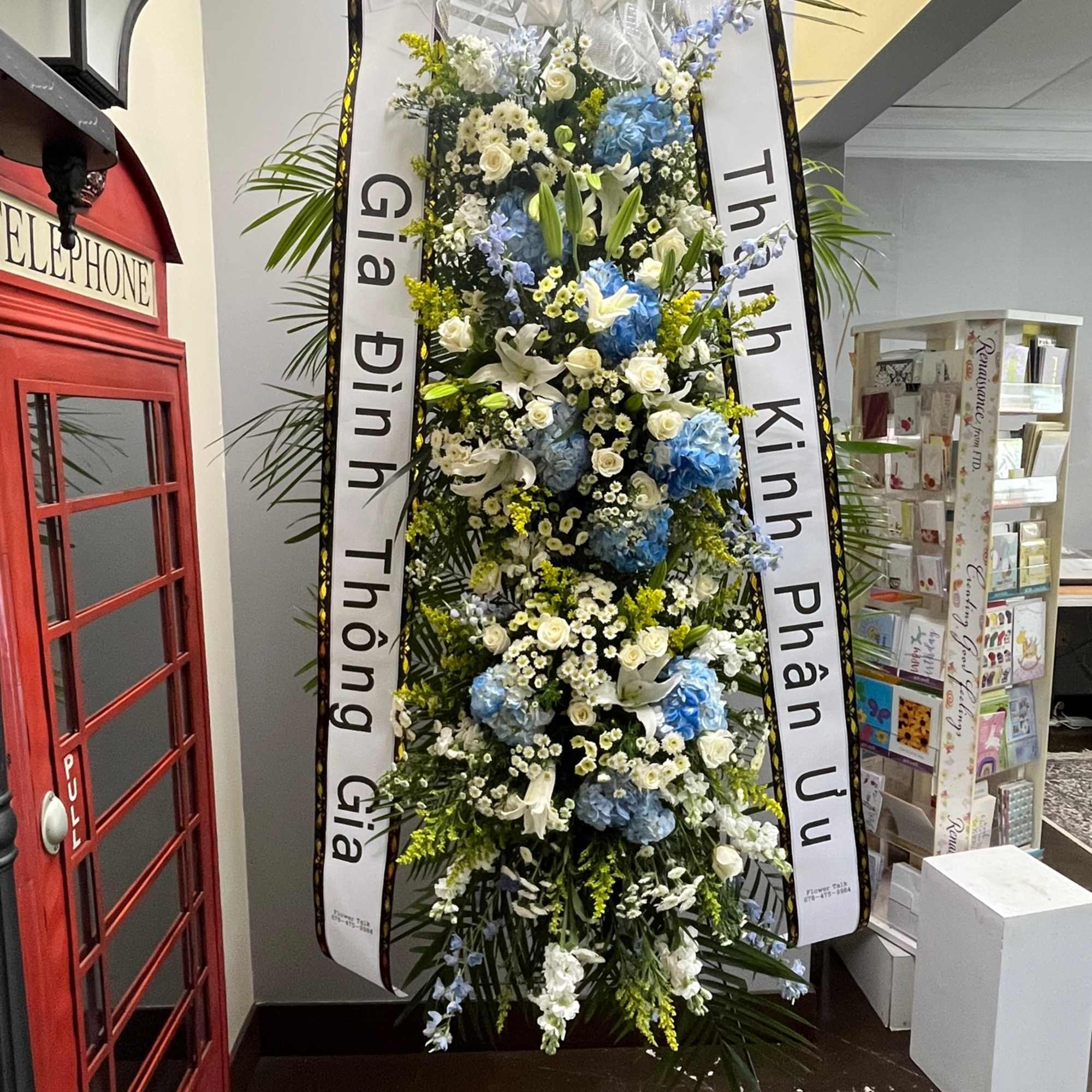 Tall funeral standing spray with blue and white flowers and condolence ribbons
