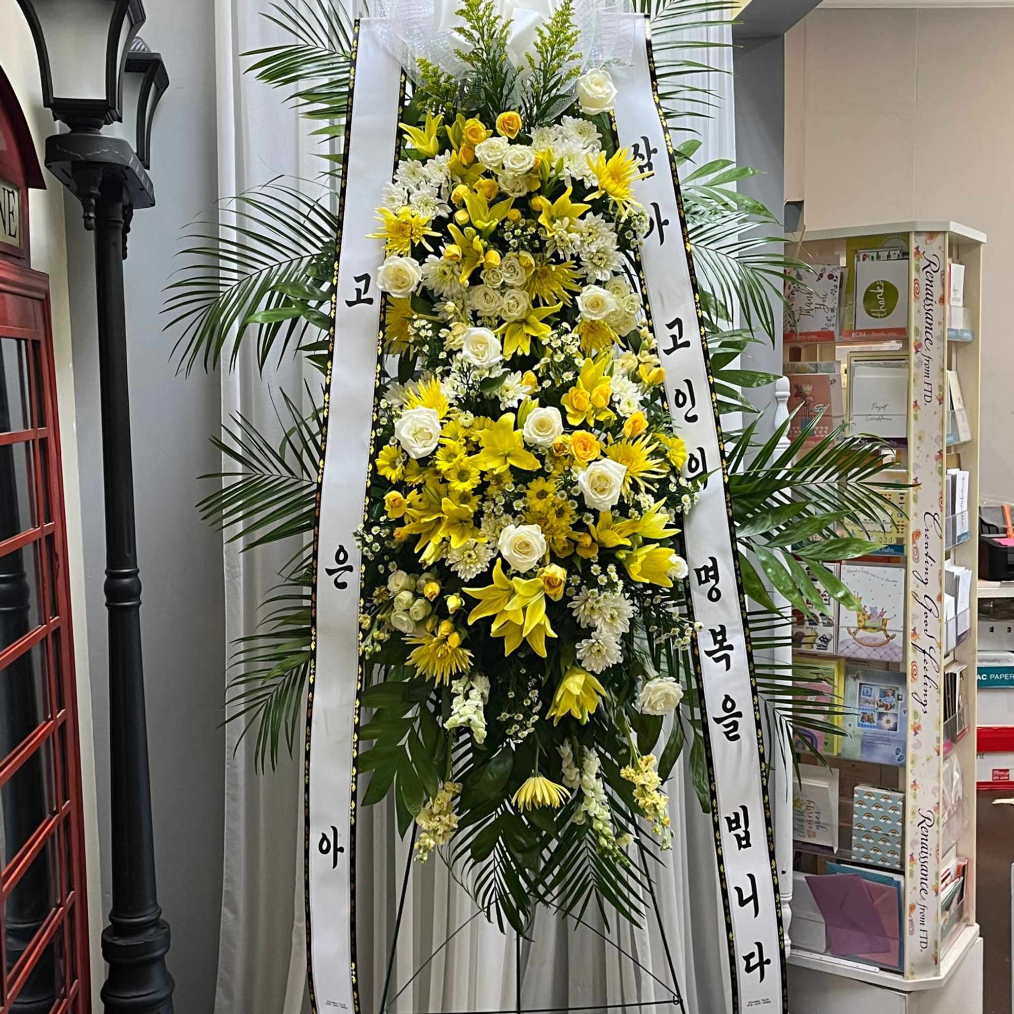 Tall standing floral wreath with yellow and white flowers on a ribboned easel