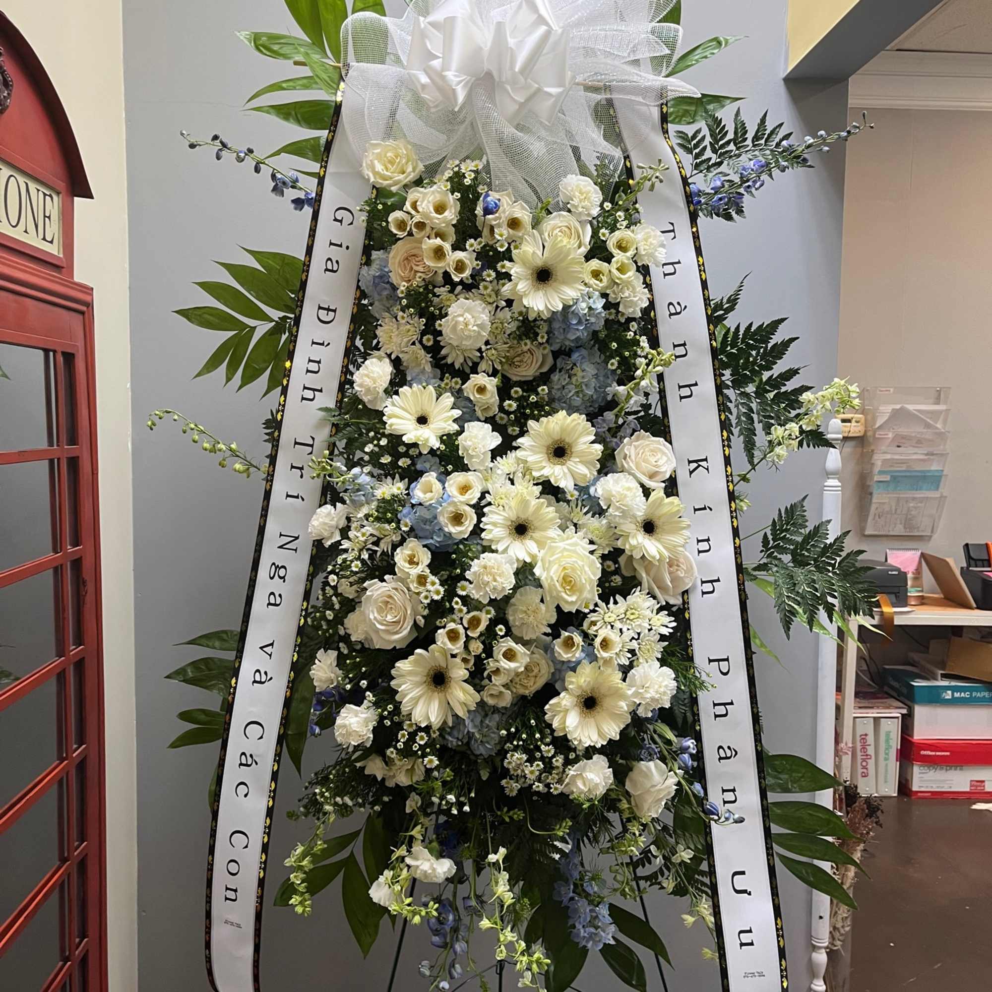 Standing funeral spray of white and pale blue flowers with ribbons