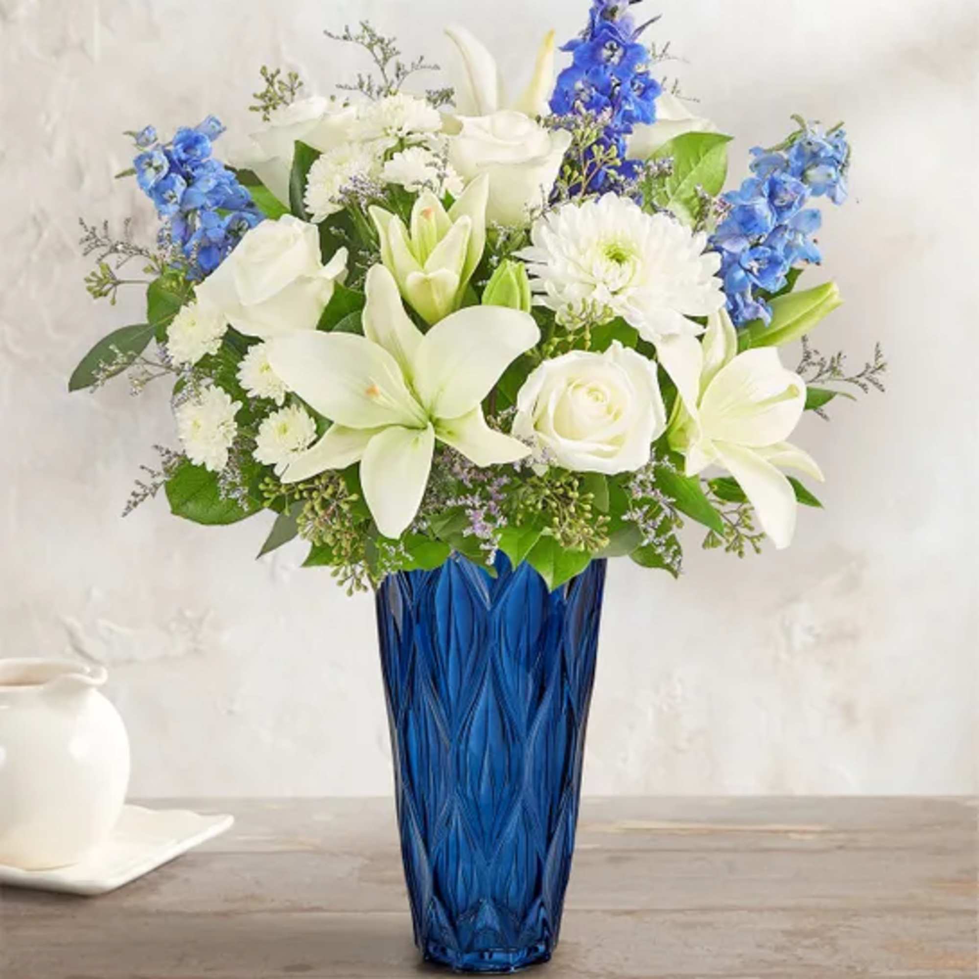 White lilies and roses in a blue glass vase with blue flowers