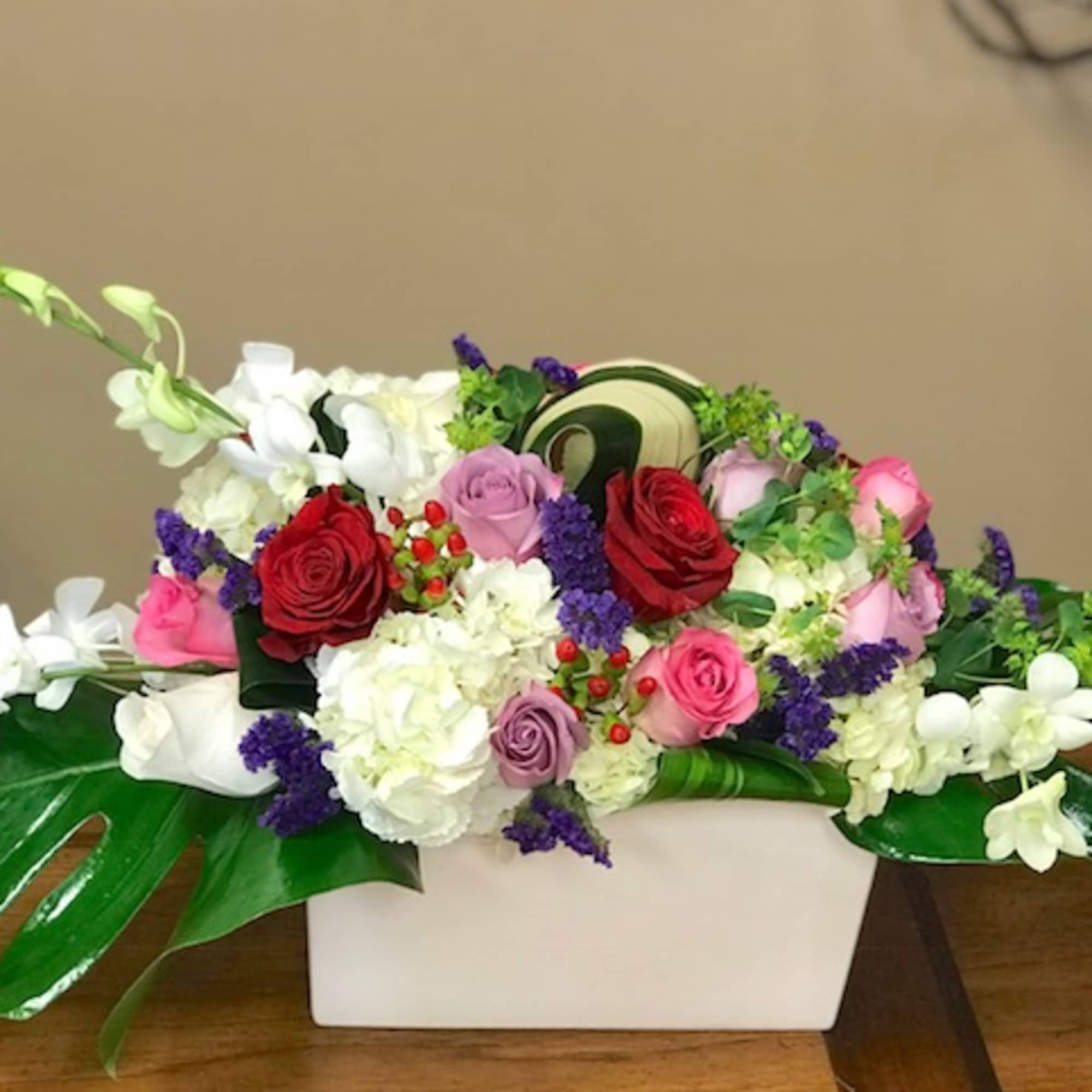 Mixed bouquet of roses, hydrangeas, and orchids in a white rectangular vase