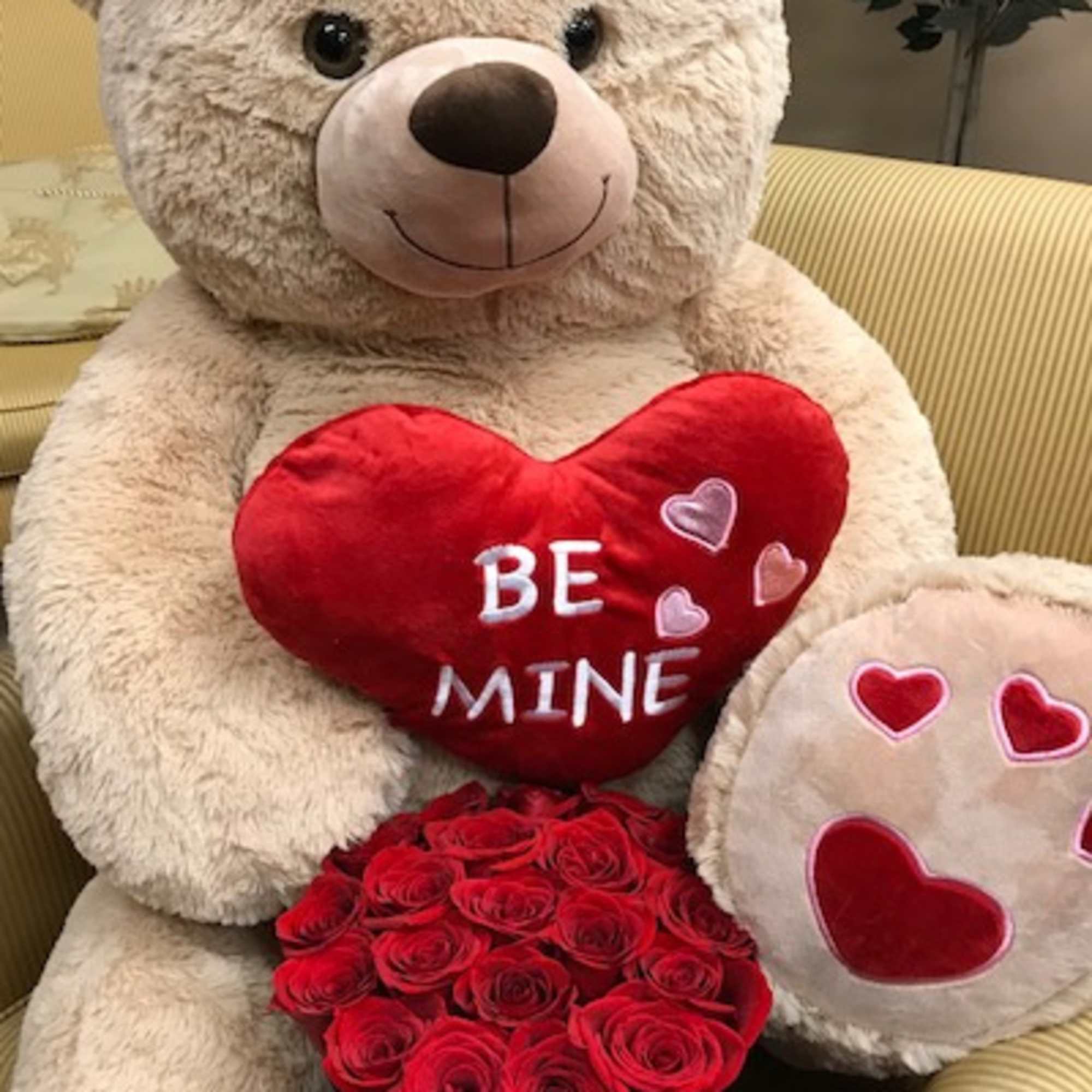 Large teddy bear holding a red heart pillow and a box of red roses