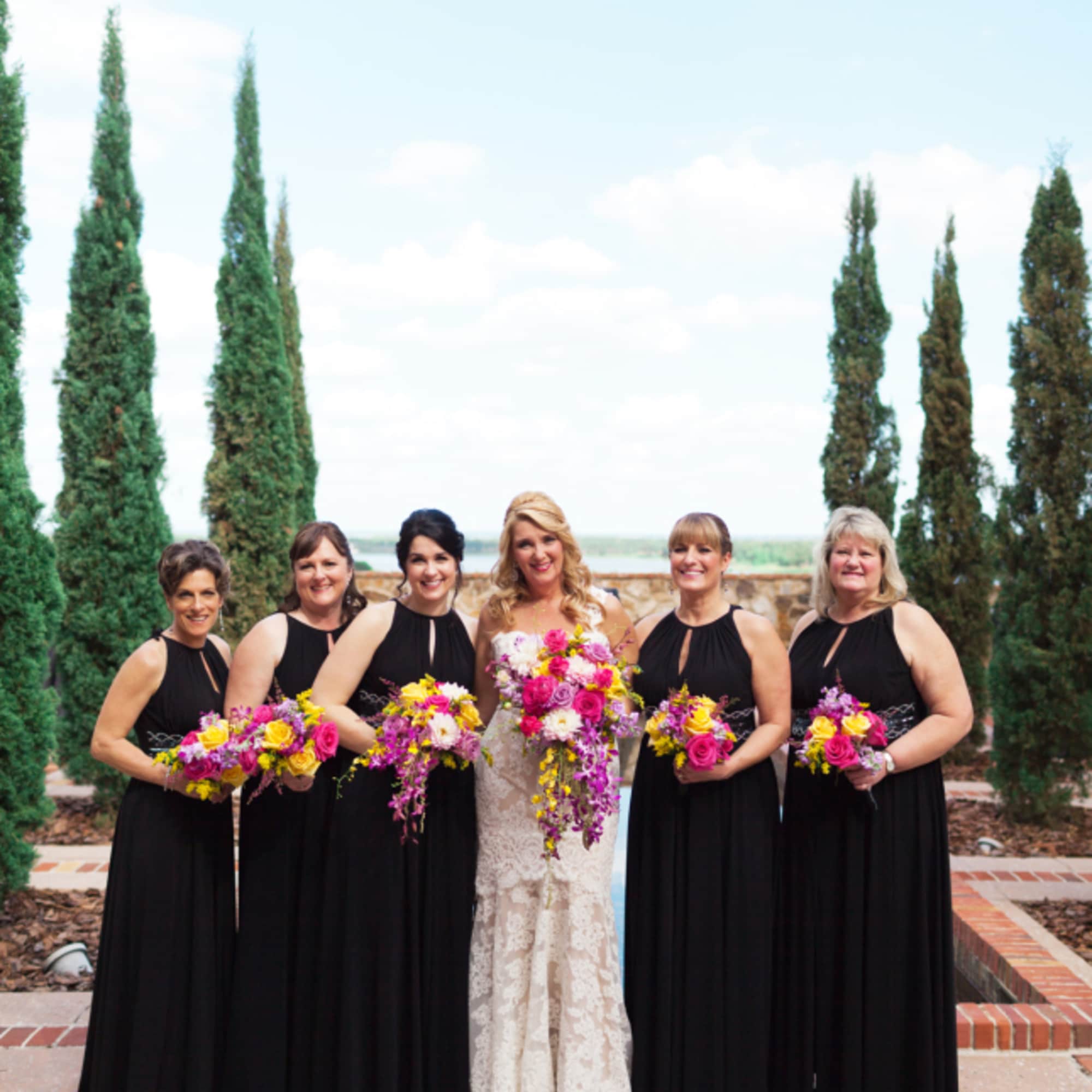 Bride and bridesmaids holding bright pink and yellow bouquets outdoors