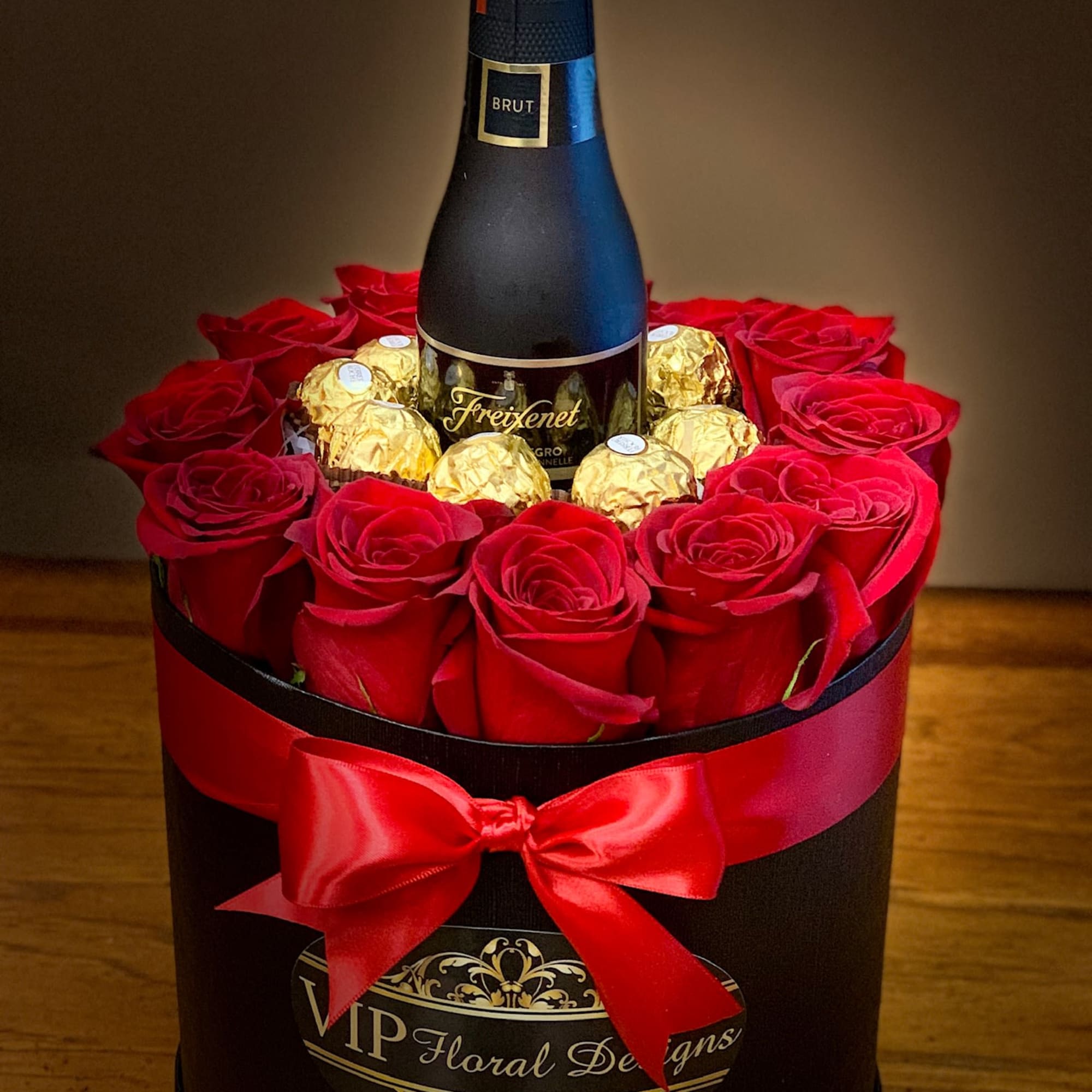 Red roses and gold chocolates around a champagne bottle in a gift box