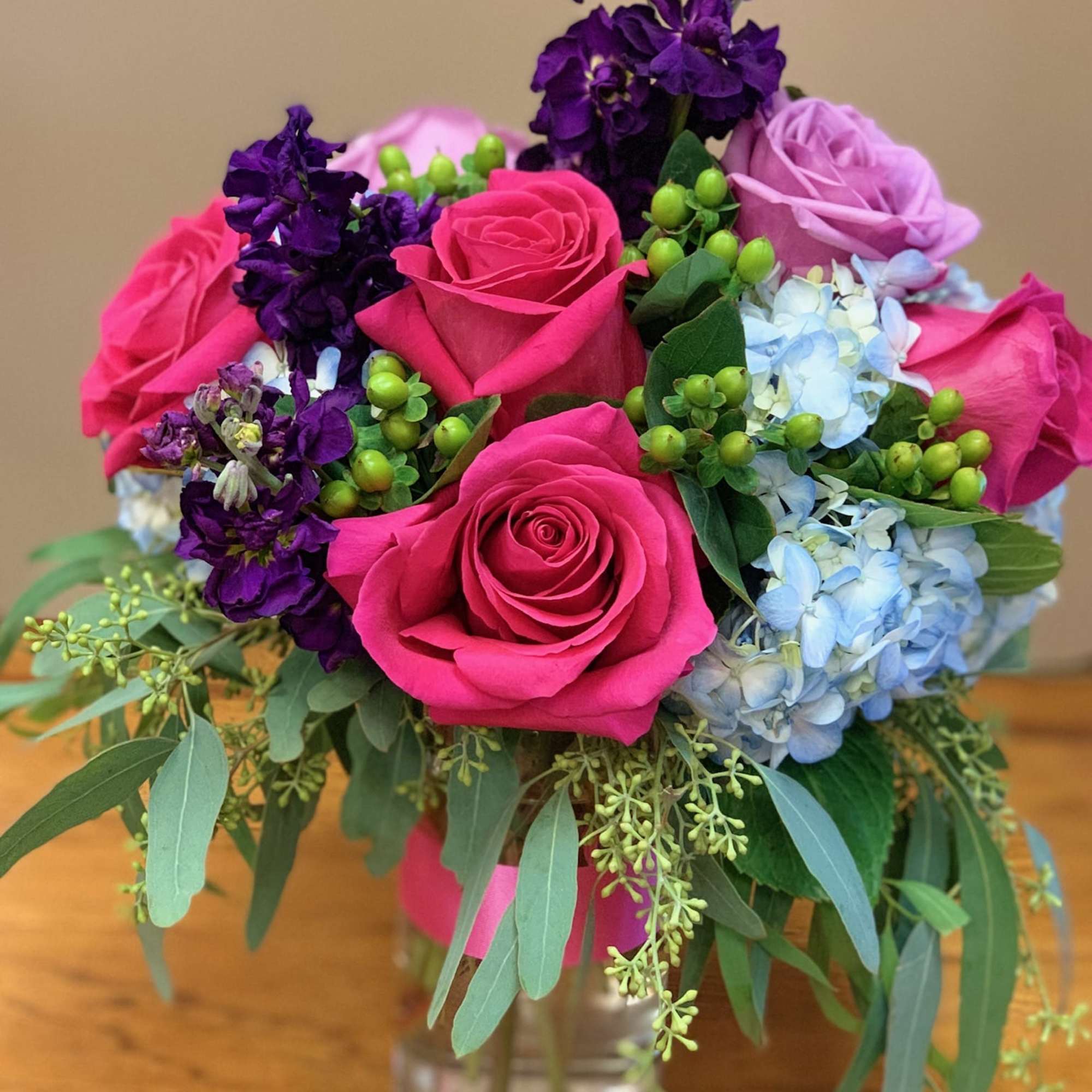 Bouquet of pink roses, purple blooms, and blue hydrangeas in a glass vase