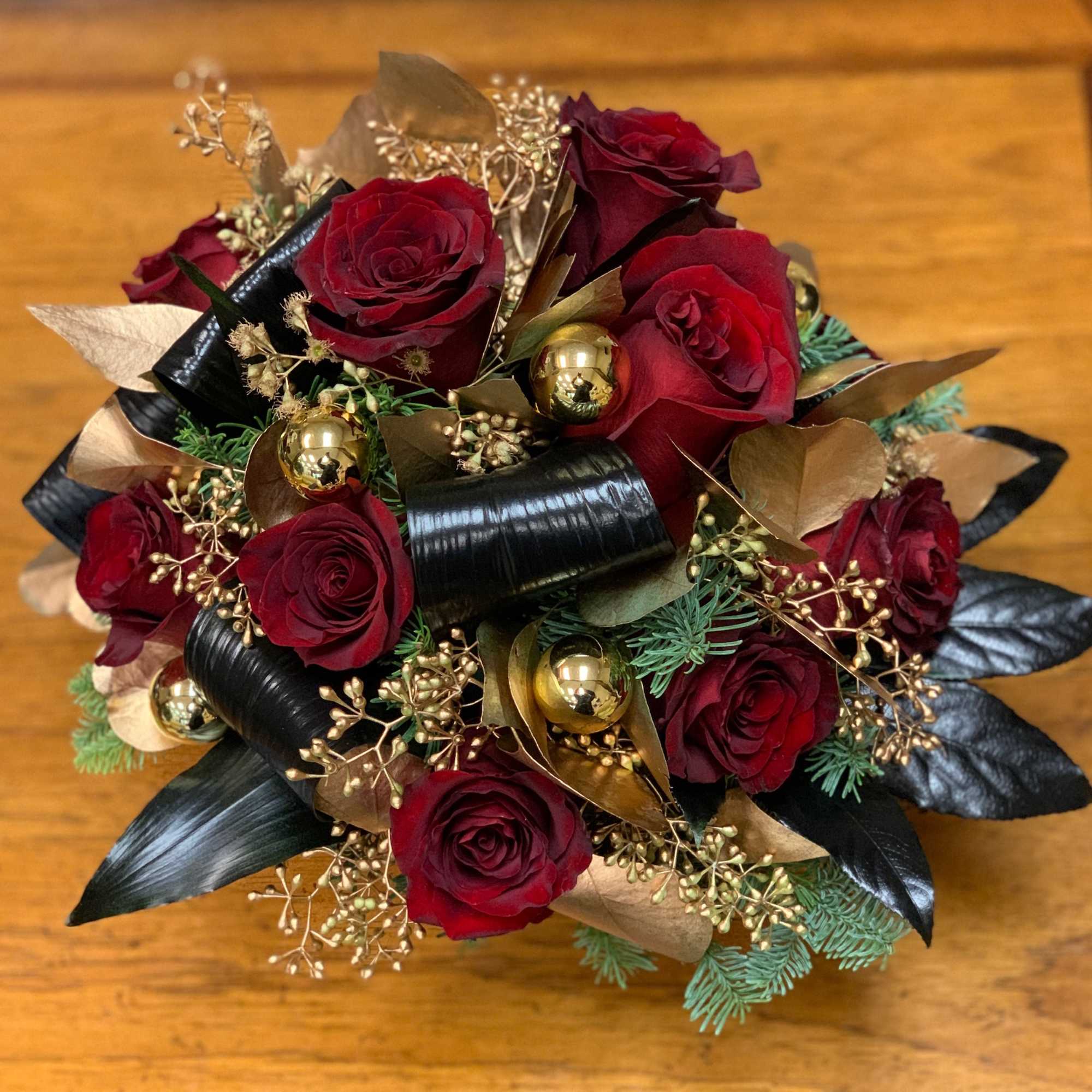 Bouquet of red roses with gold accents and black ribbon on a wooden surface