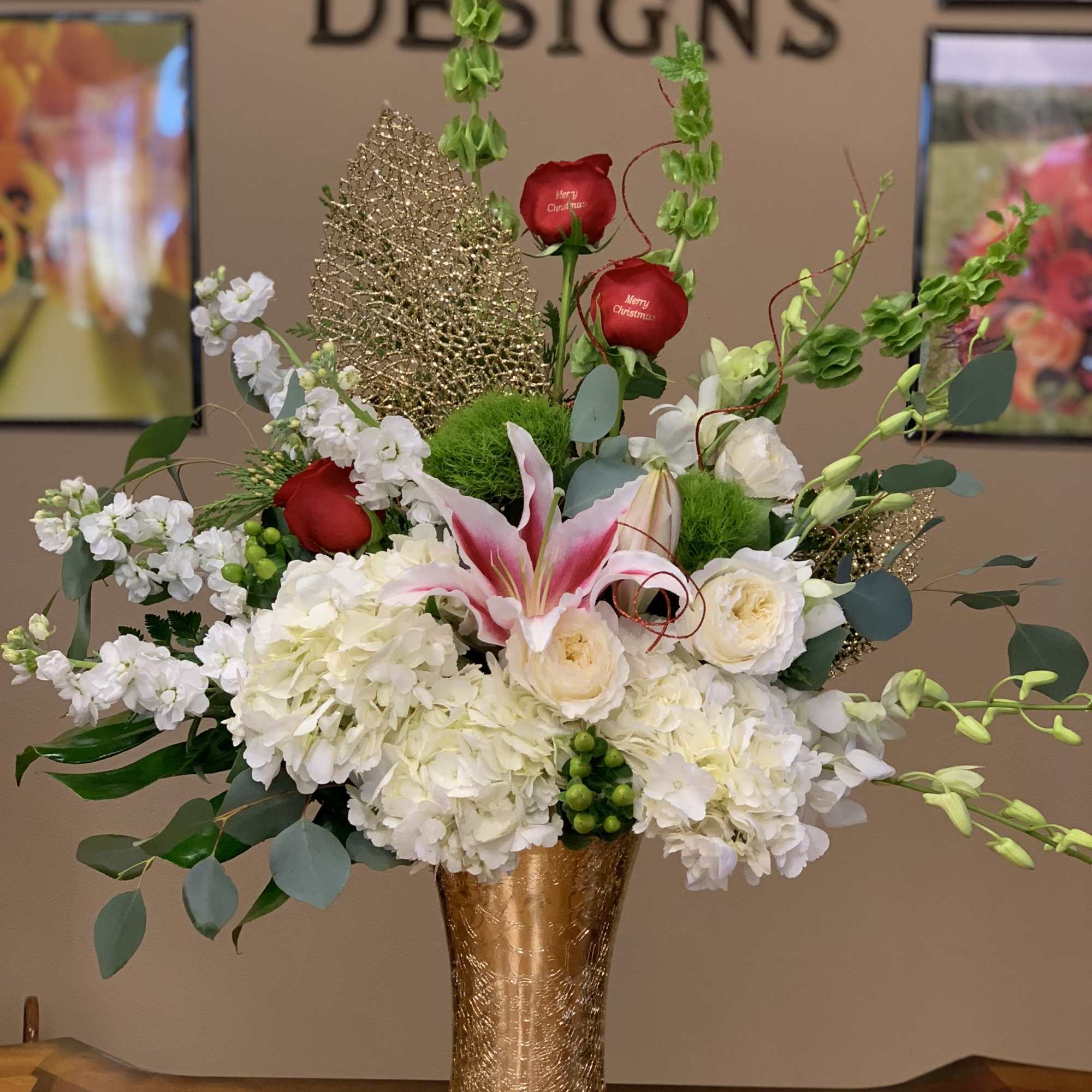 Tall floral arrangement with white blooms, red roses, and pink lilies in a gold vase
