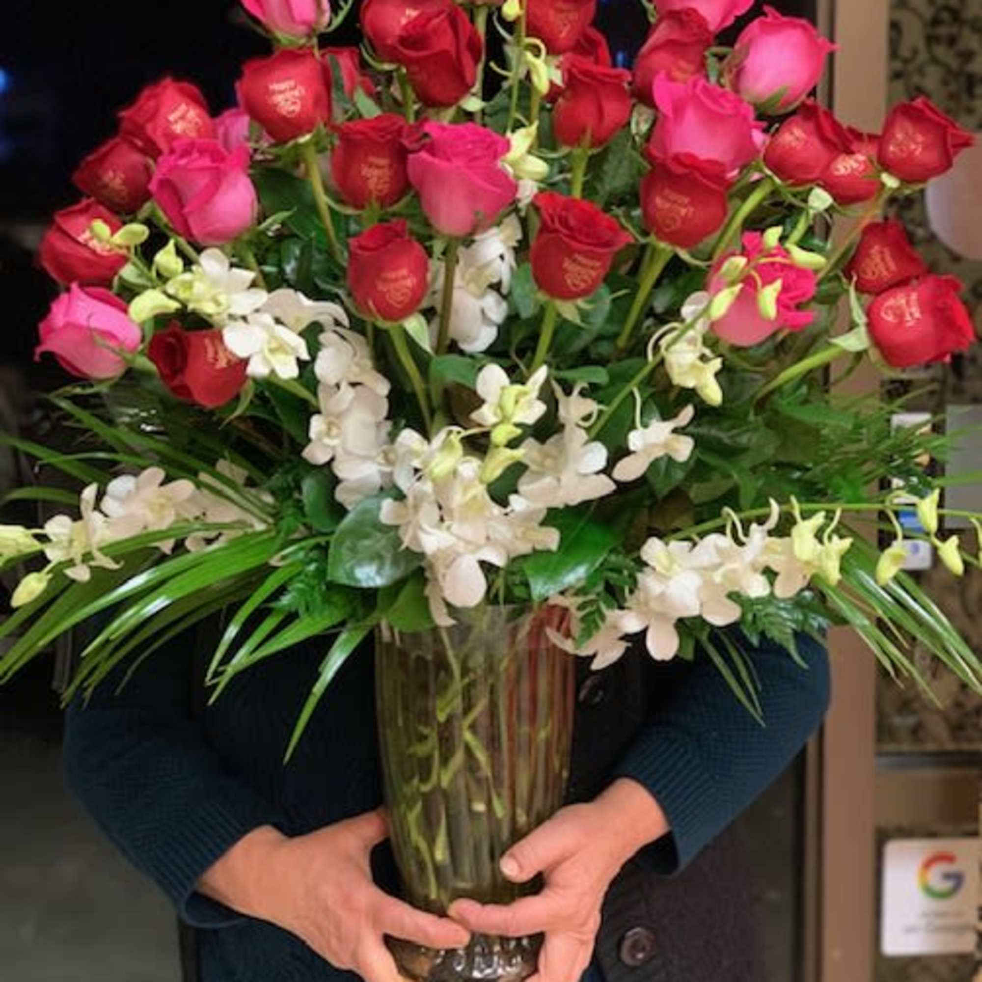 Large bouquet of red and pink roses with white orchids in a glass vase