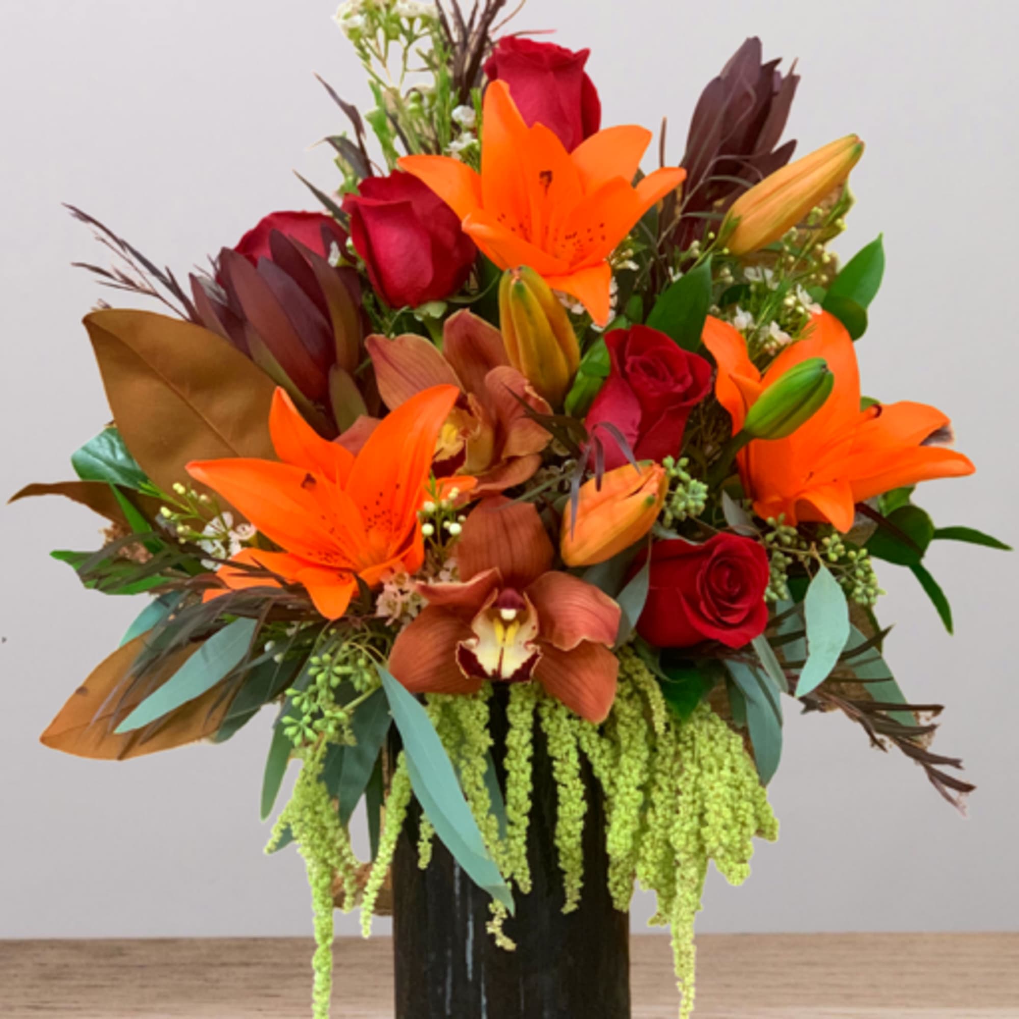 Bouquet of orange lilies and red roses in a black vase