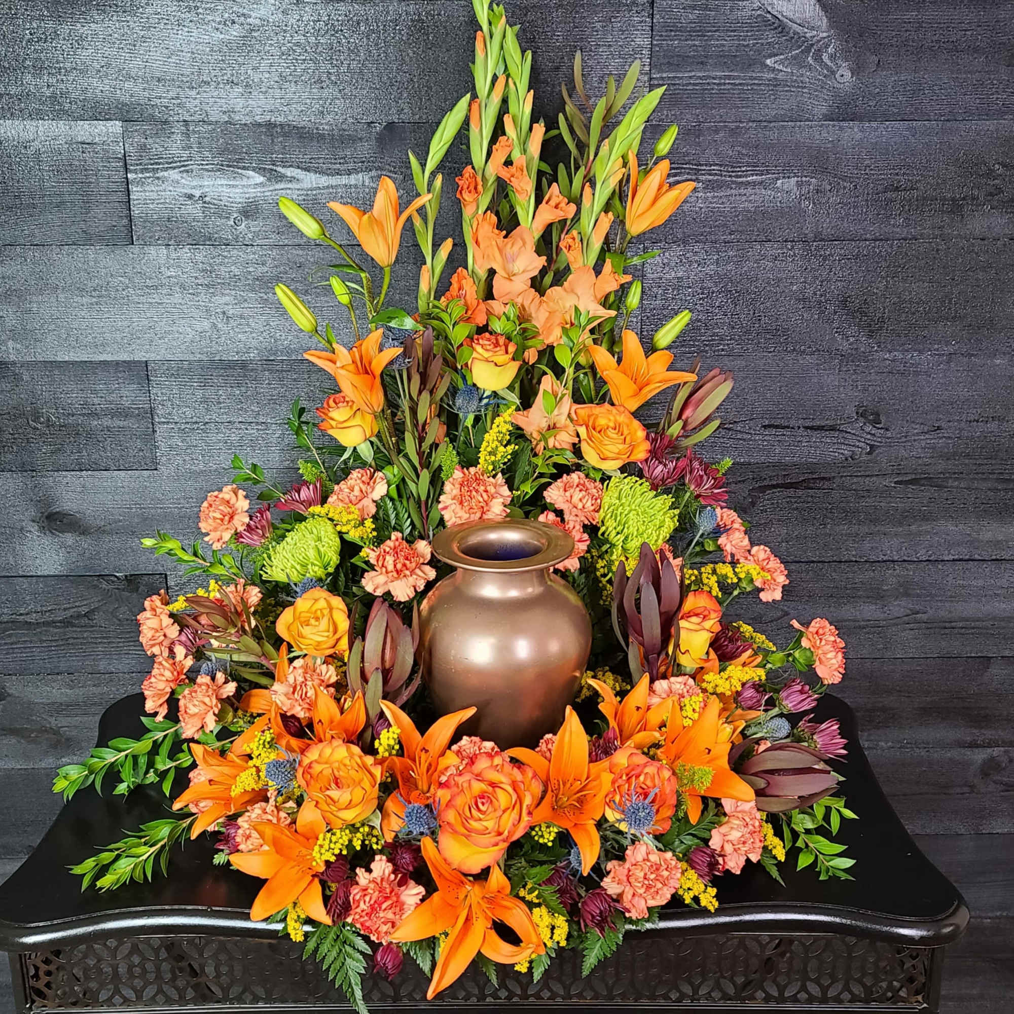 Orange lilies and roses arranged around a bronze urn centerpiece