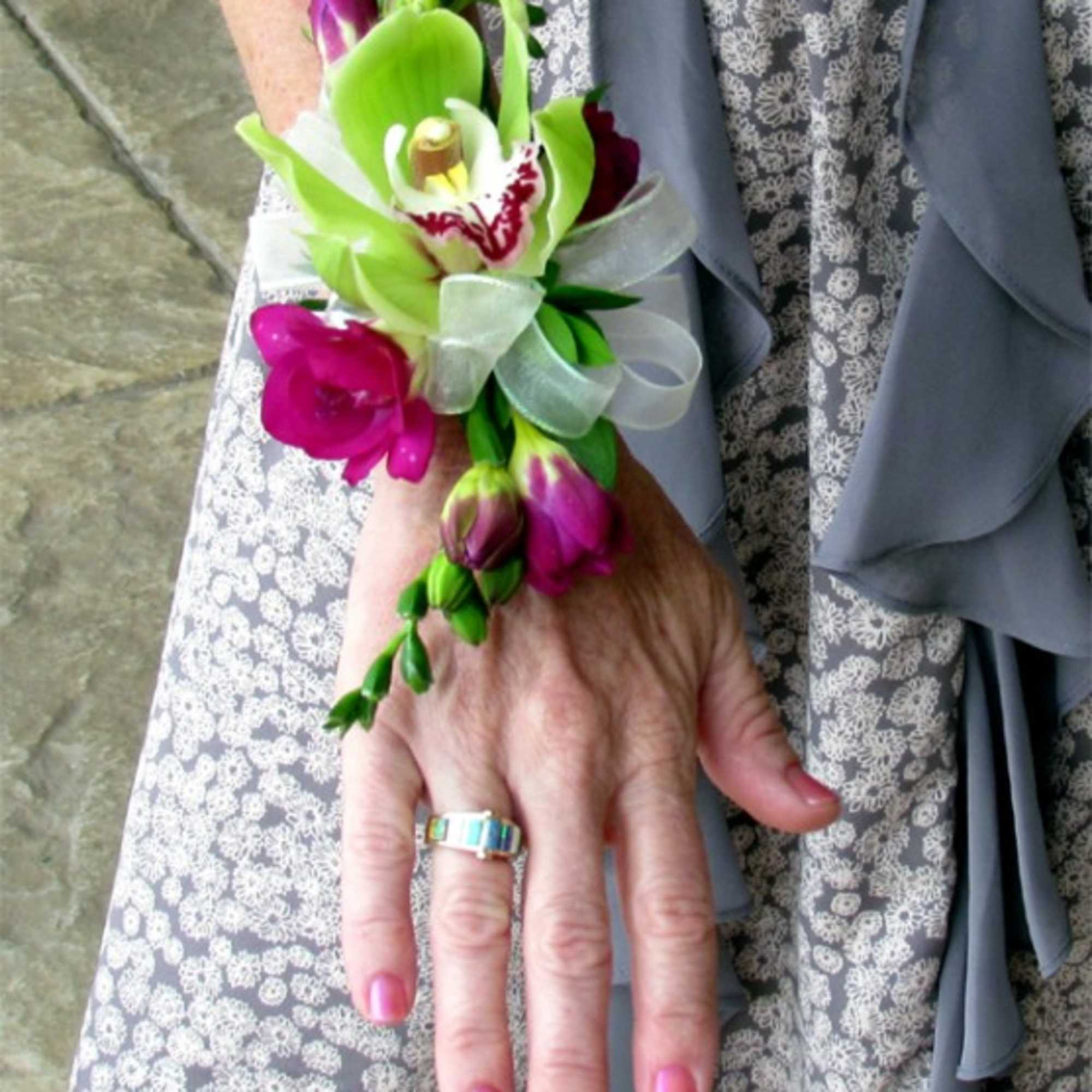 Wrist corsage with green and magenta orchids and a white ribbon