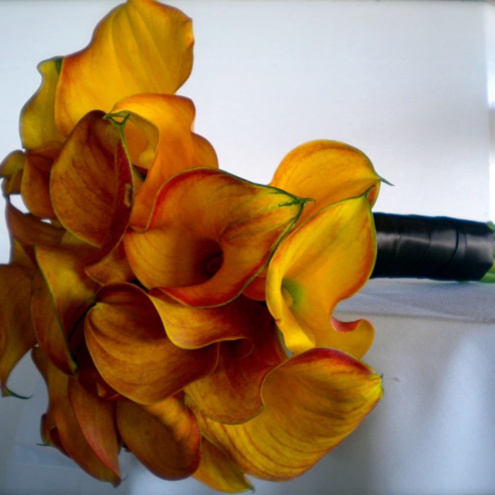 Bouquet of orange and yellow calla lilies with a black wrapped handle