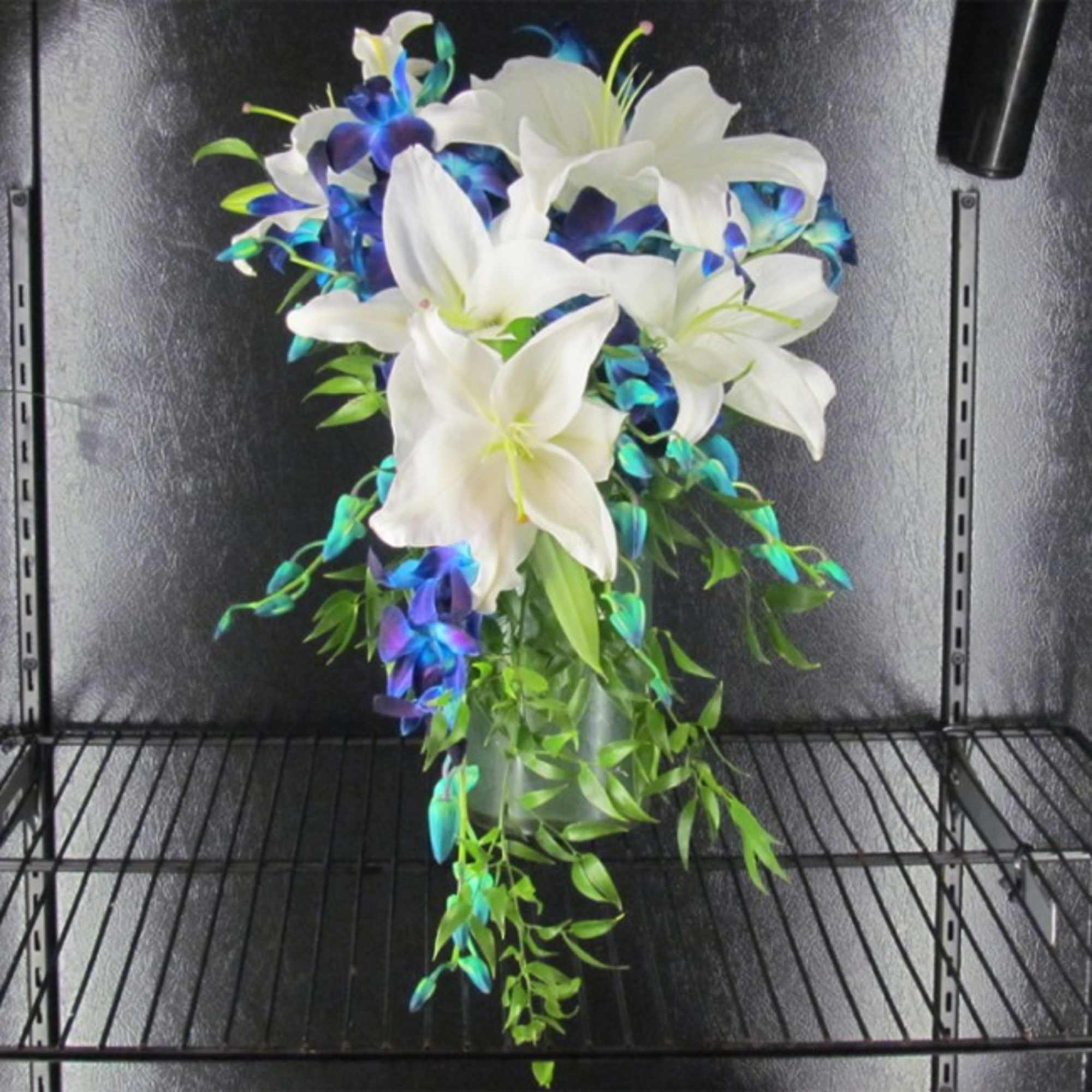 White lilies with blue-purple orchids in a glass vase