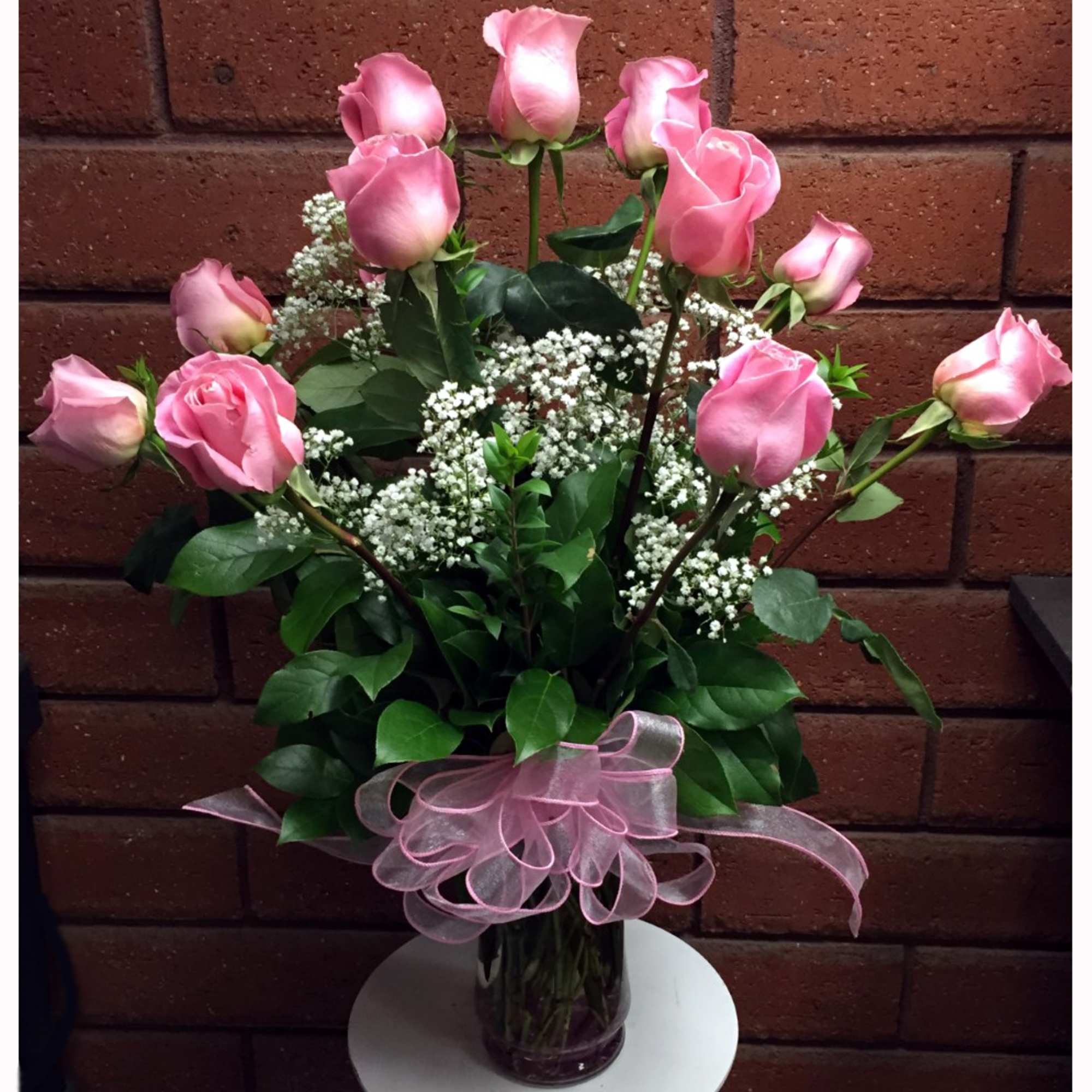 Pink roses arranged in a glass vase with baby's breath and a pink ribbon
