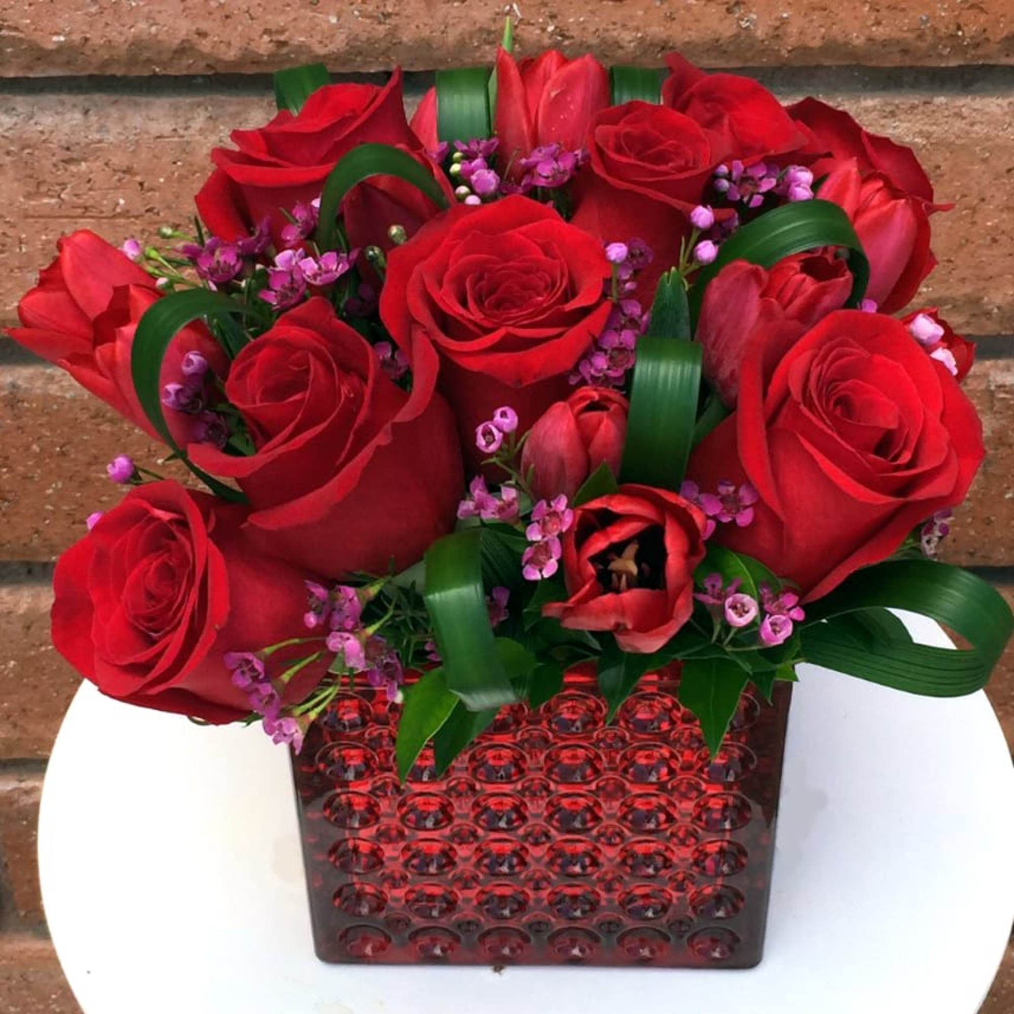 Red roses and tulips in a red textured vase with purple filler flowers
