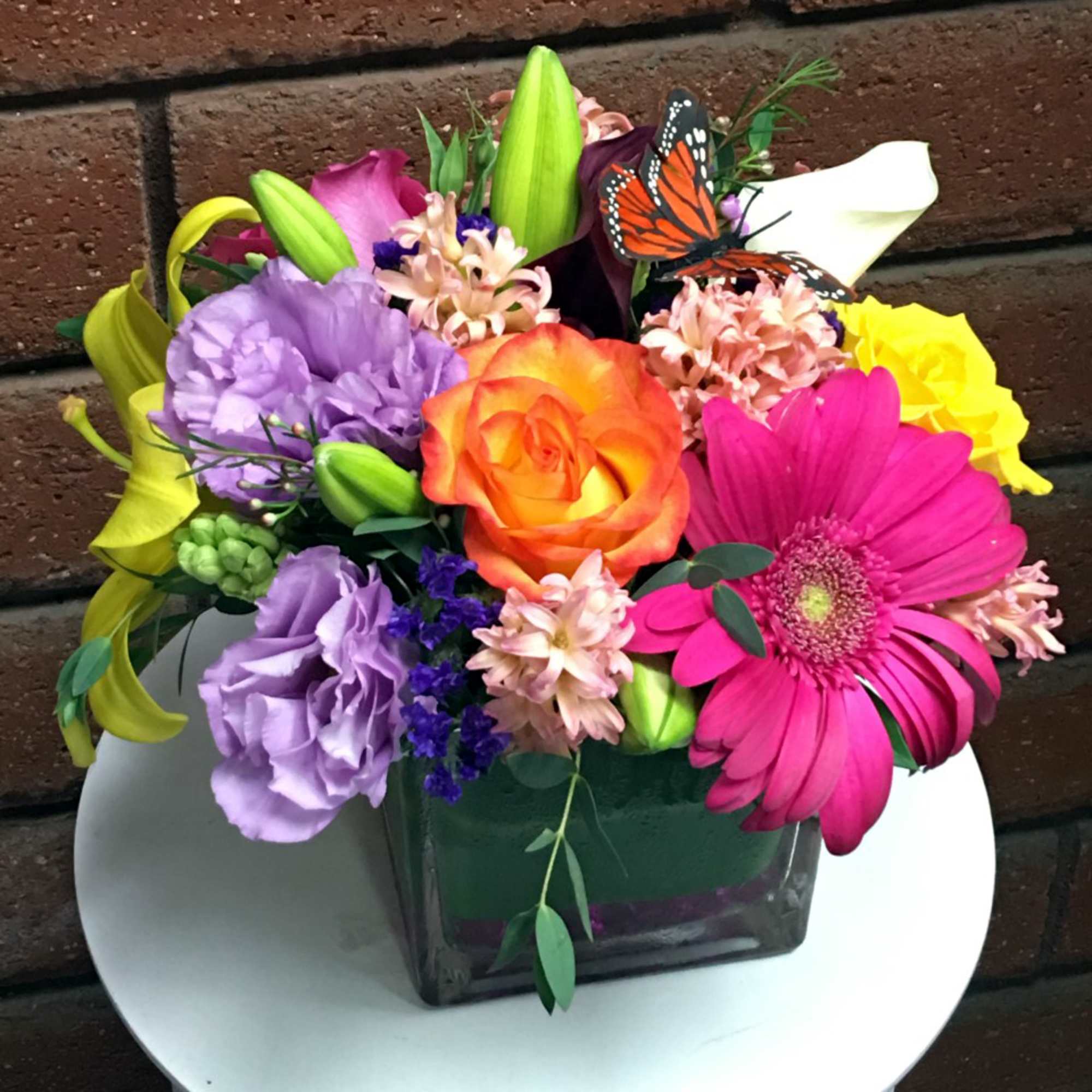 Colorful mixed bouquet in a square glass vase with a butterfly accent