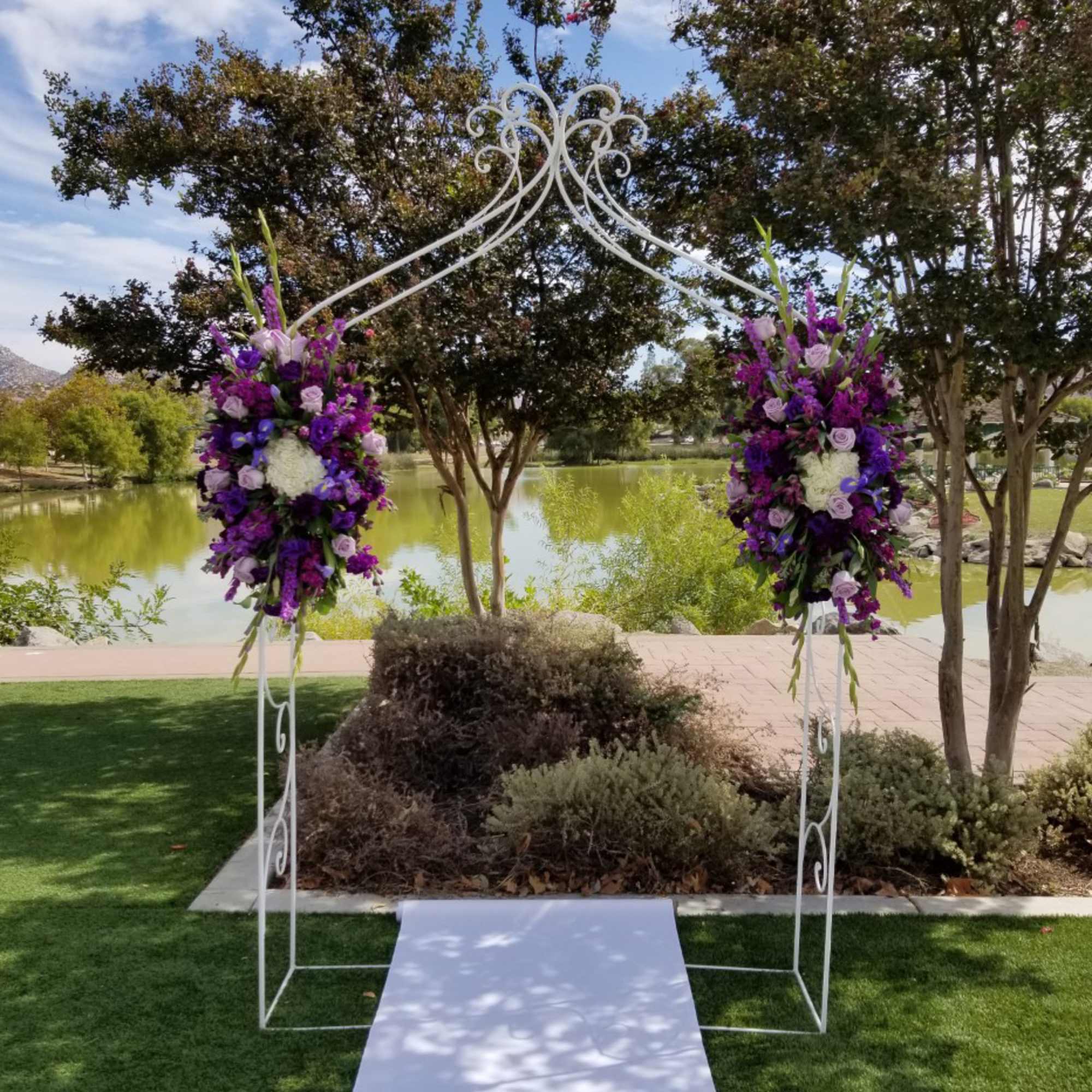 Purple floral wedding arch with white metal frame beside a white aisle runner