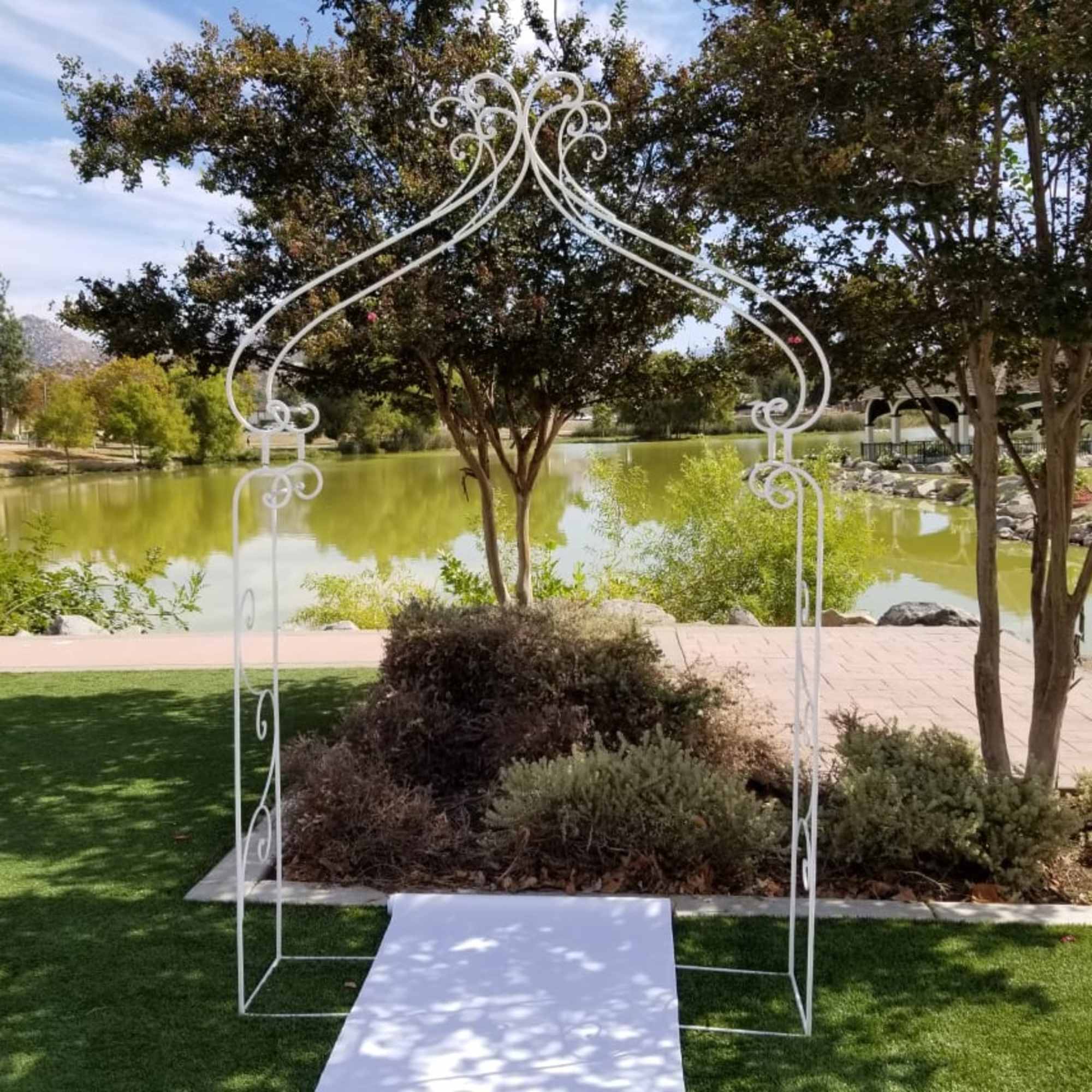 White decorative wedding arch over a white aisle runner by a pond