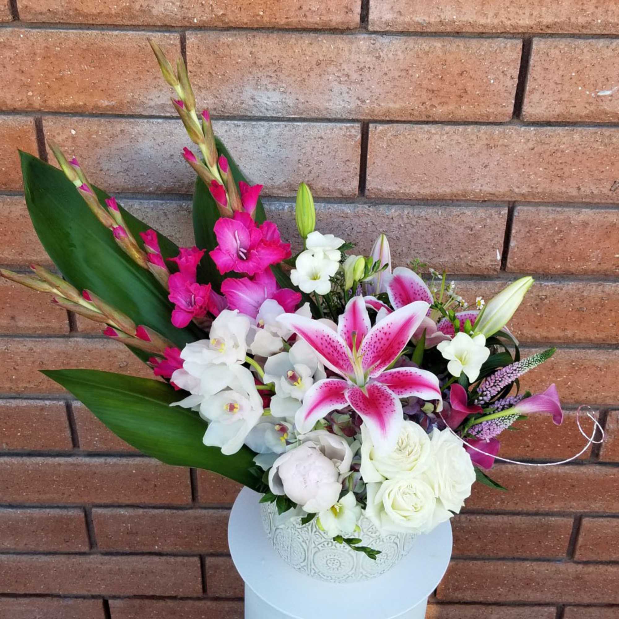 Pink lilies and white orchids in a white vase with broad leaves