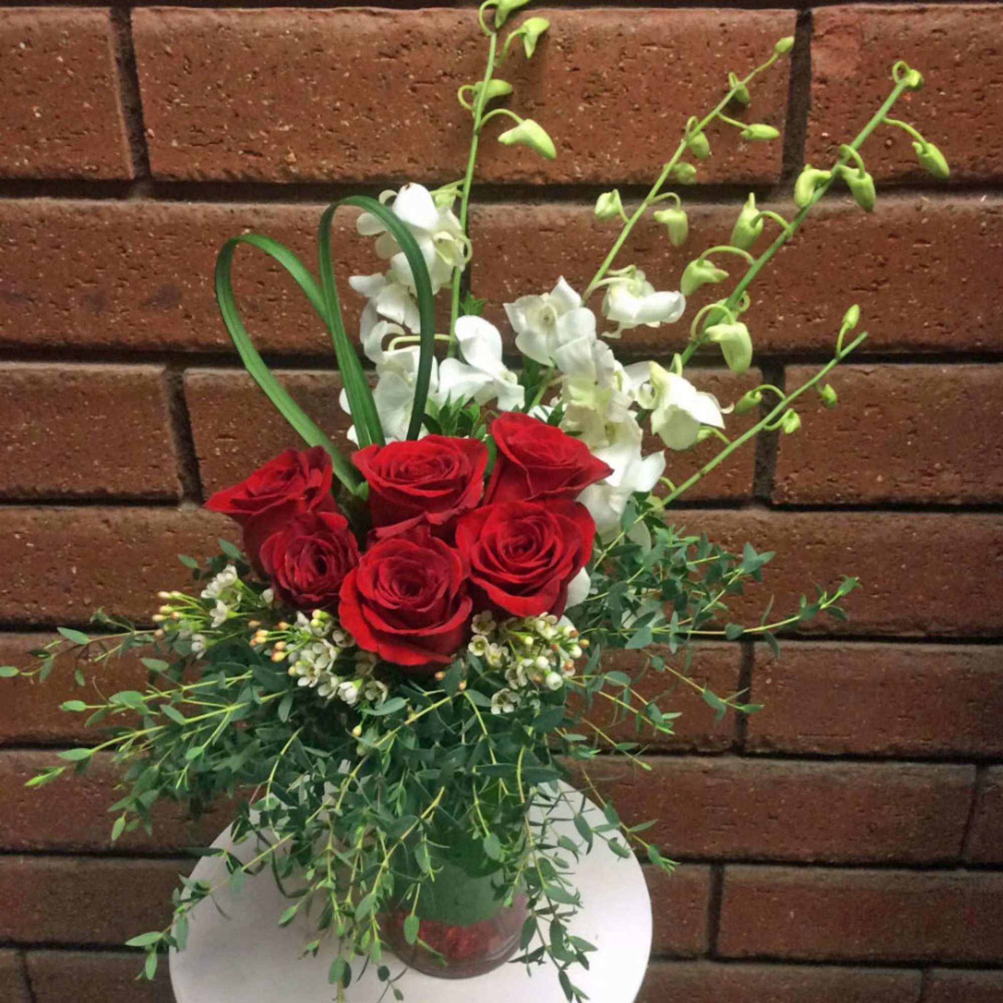 Red roses and white orchids in a glass vase with greenery