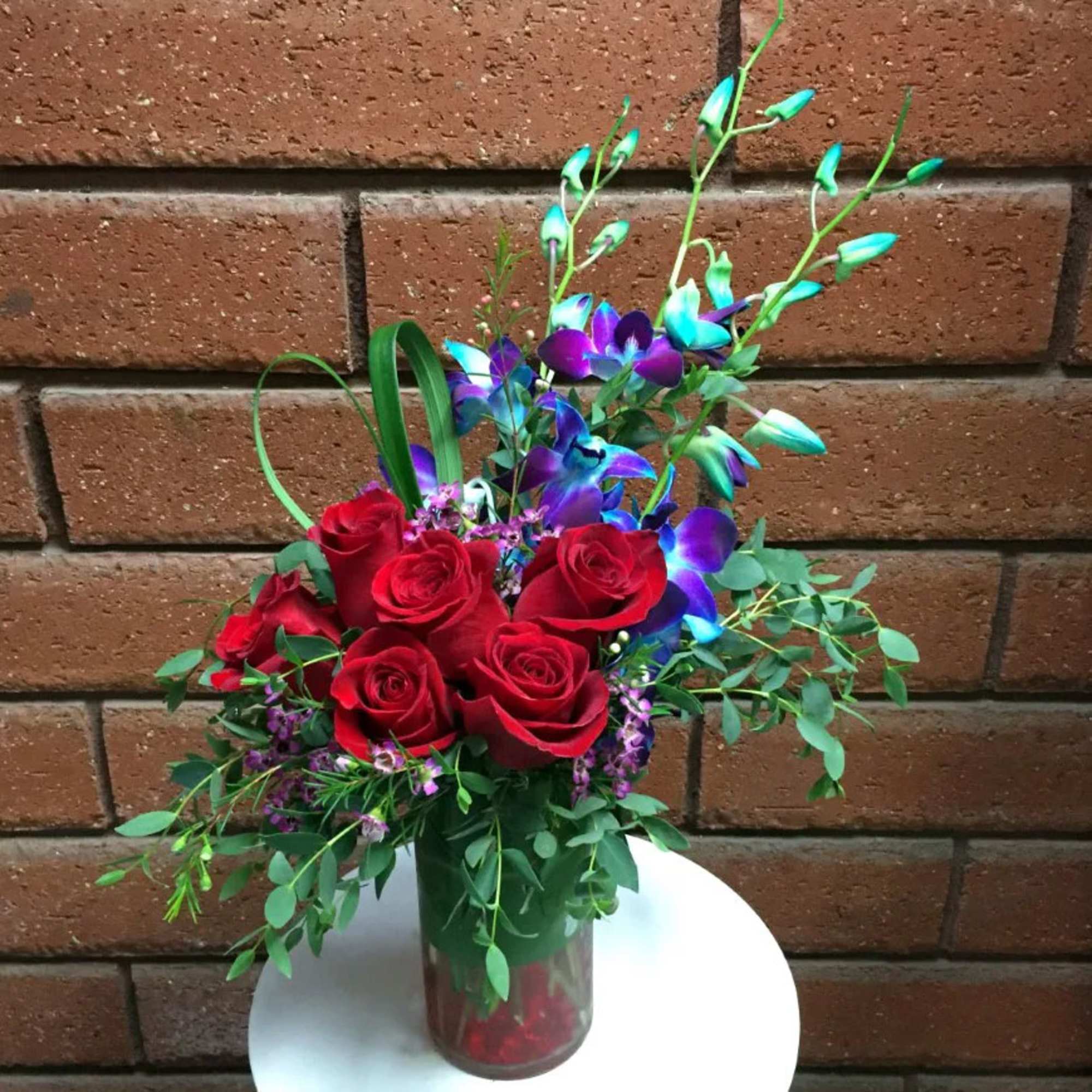 Red roses and blue-purple orchids in a glass vase