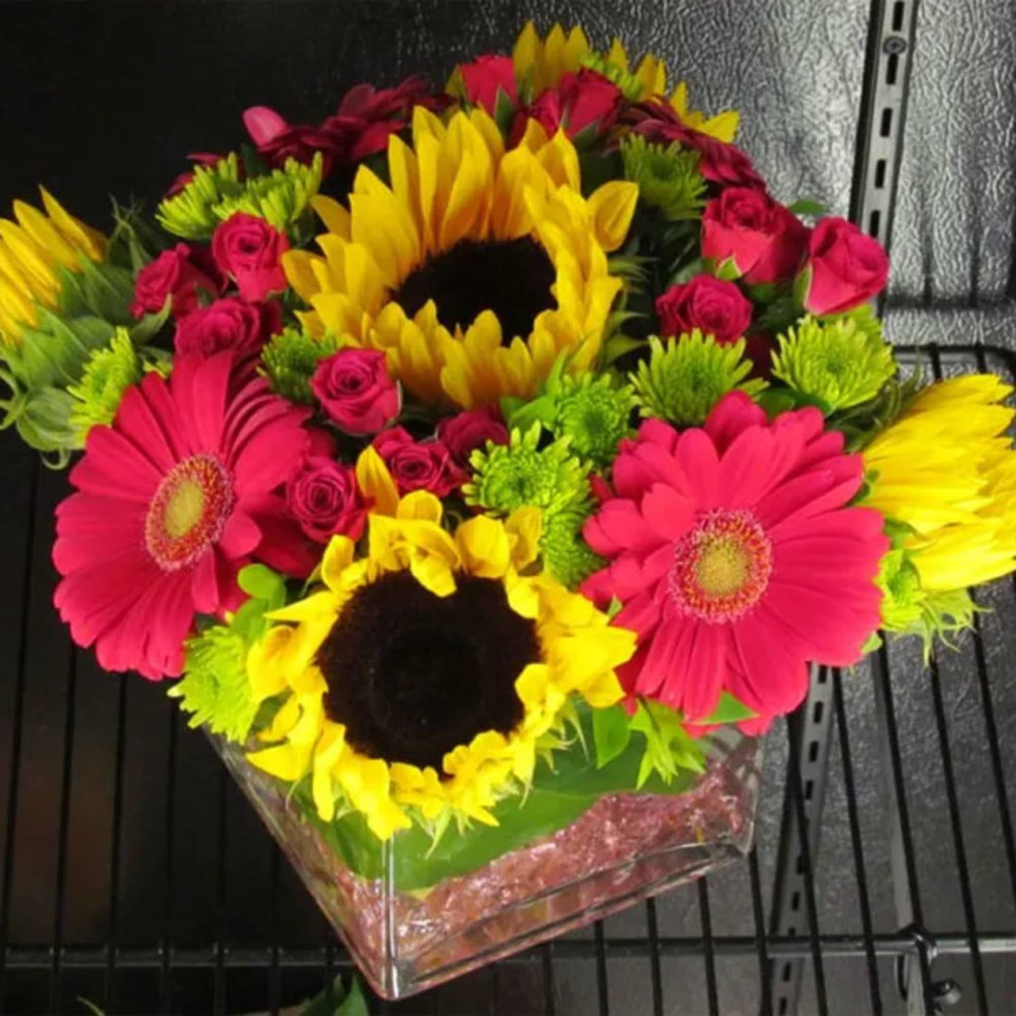 Bright bouquet with sunflowers, pink gerberas, and small roses in a clear vase