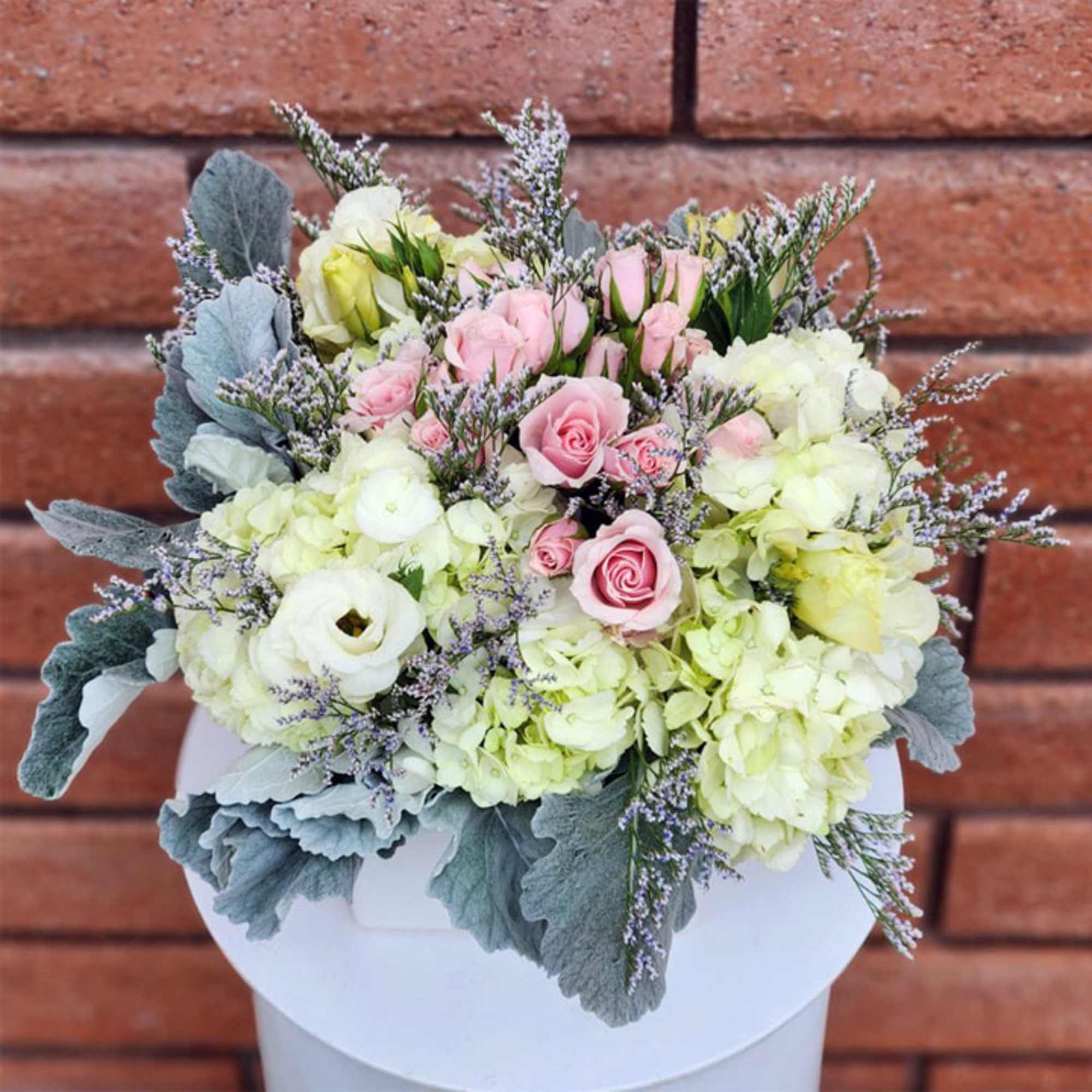 Pink roses and white hydrangeas in a white vase with silvery foliage