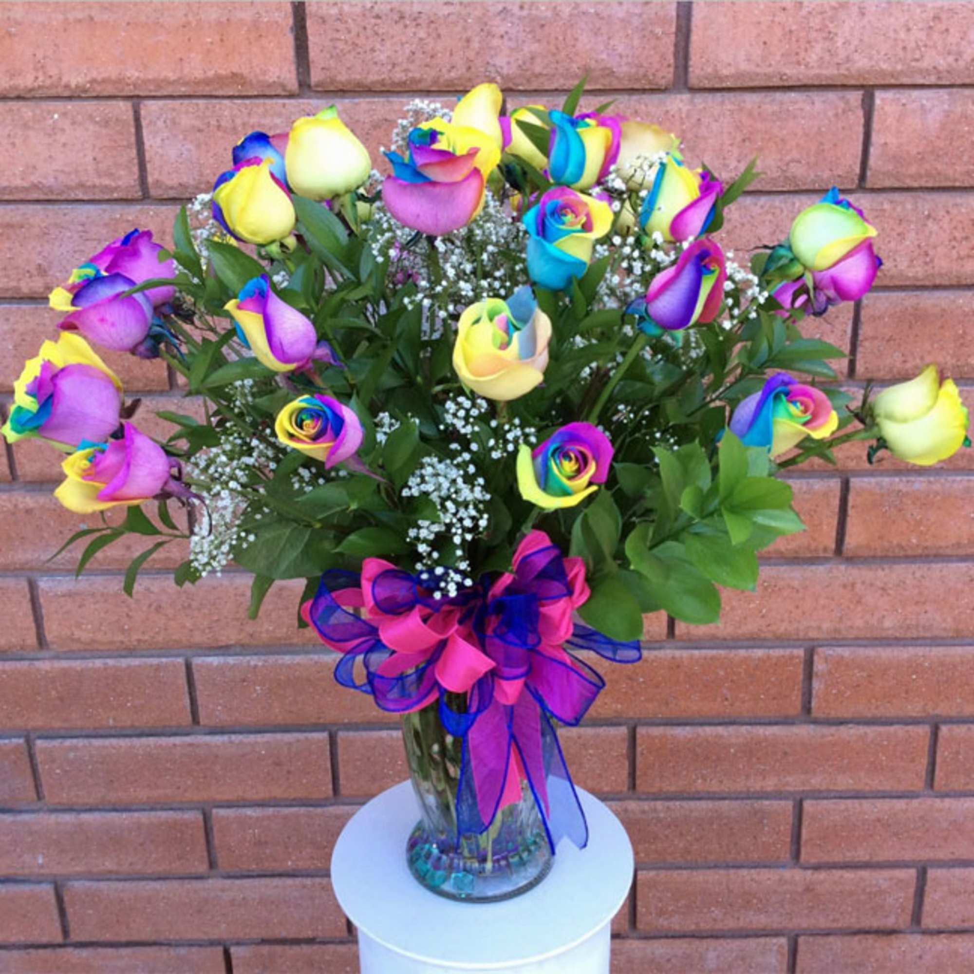 Rainbow-colored roses in a glass vase with a pink and blue ribbon
